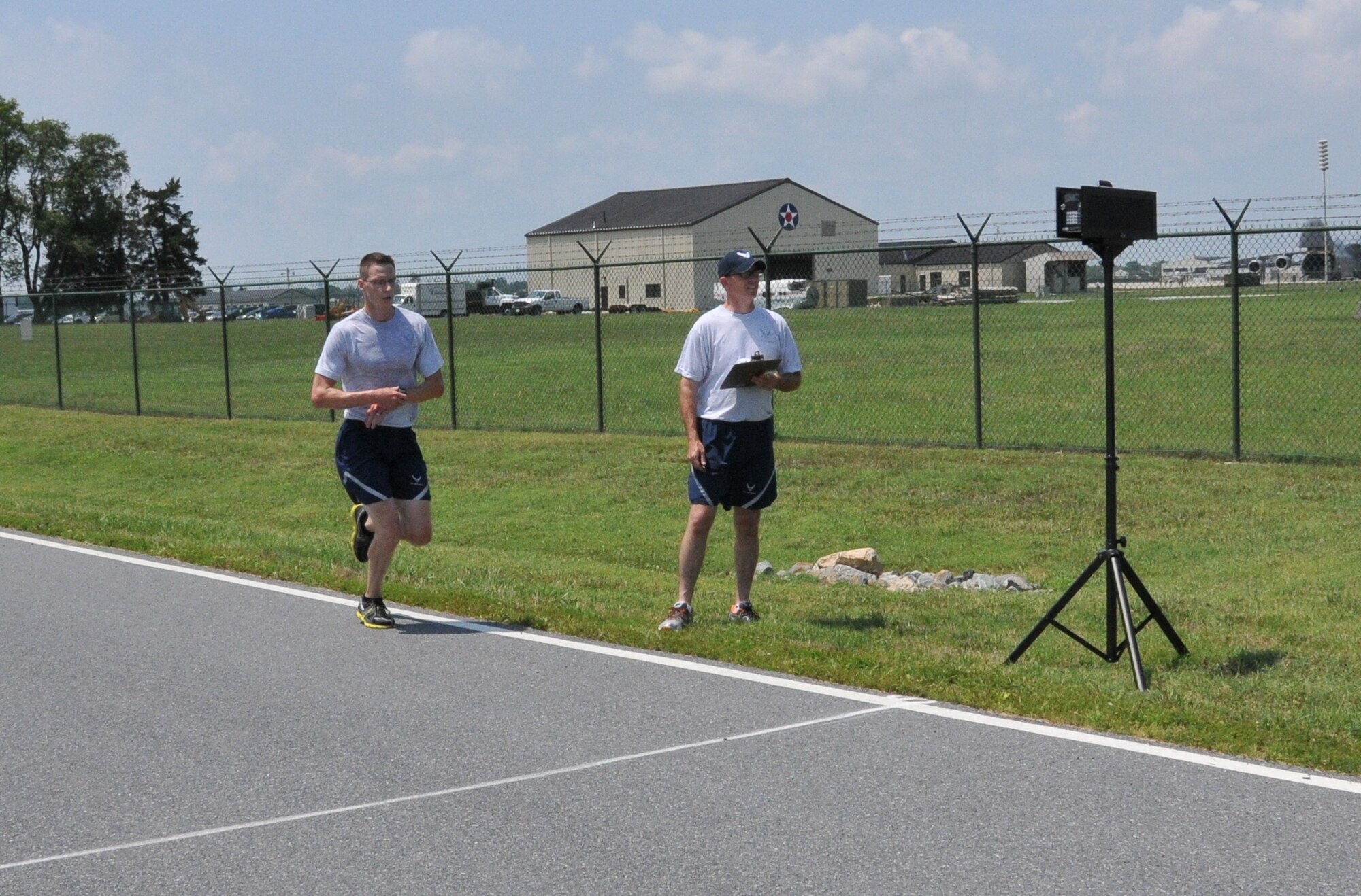 Tech. Sgt. Sean McGahuey (left), 512th Communications Operations Flight, approaches the finish line during a 5K race during Wingman Day held July 12, 2014 at Dover Air Force Base, Del. Chief Master Sgt. Bryan Ford, 512th Maintenance Group, recorded McGahuey's time at 17:22. (U.S. Air Force photo/Senior Airman Joe Yanik)