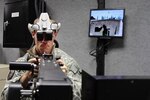 Army Staff Sgt. James Stanfield with Company F, 634th Brigade Support Battalion, mans the turret in Sparta Training Area's new Virtual Vehicle Simulator, a state-of-the-art combat simulator capable of putting over 25 Soldiers into the same massive virtual environment. The VVT allows Stanfield to see into a custom-made scenario (his view is shown on the screen behind him) while still operating realistic equipment like vehicle controls and mock machine guns.