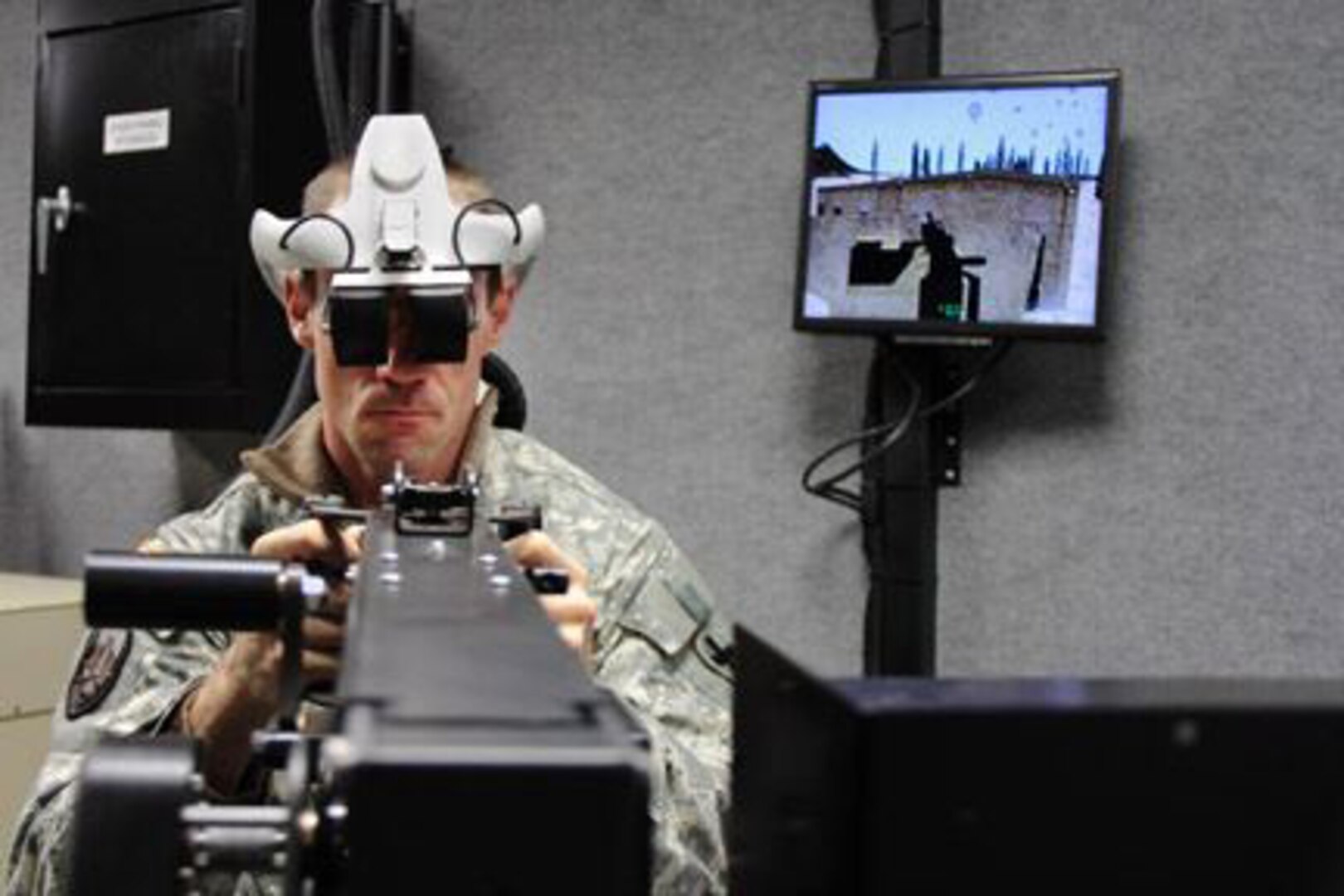 Army Staff Sgt. James Stanfield with Company F, 634th Brigade Support Battalion, mans the turret in Sparta Training Area's new Virtual Vehicle Simulator, a state-of-the-art combat simulator capable of putting over 25 Soldiers into the same massive virtual environment. The VVT allows Stanfield to see into a custom-made scenario (his view is shown on the screen behind him) while still operating realistic equipment like vehicle controls and mock machine guns.