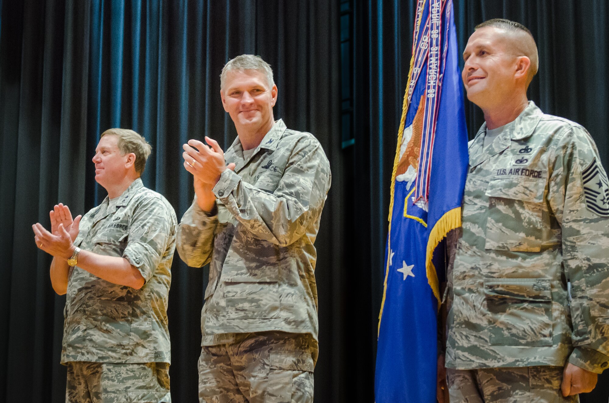 Chief Master Sgt. Ray Dawson (right), command chief master sergeant for the Kentucky Air National Guard’s 123rd Airlift Wing, holds the wing guidon during an award ceremony at Louisville Male High School in Louisville, Ky., July 13, 2014, as Maj. Gen. Edward W. Tonini (left), Kentucky’s adjutant general, and Col. Barry Gorter, wing commander, applaud. The ceremony was held to present the wing with its 16th Air Force Outstanding Unit Award. (U.S. Air National Guard photo by Senior Airman Joshua Horton)