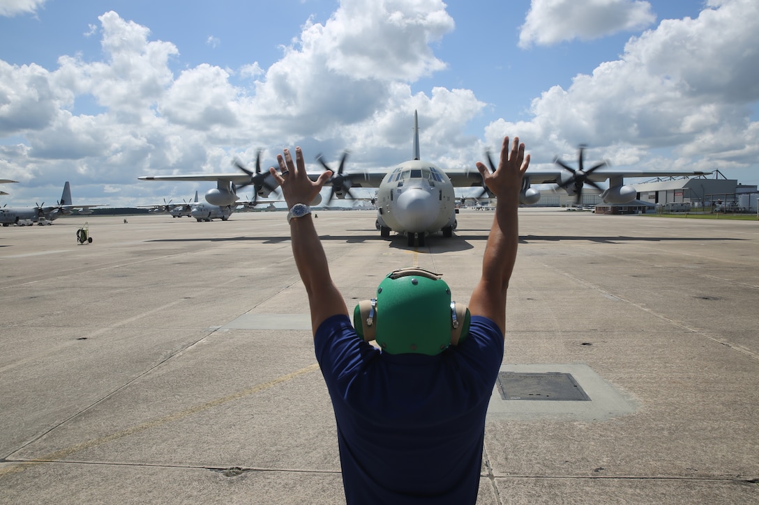 Mike Martinez signals to stop a Kuwait Air Force KC-130J Hercules on the Marine Corps Air Station Cherry Point flight line July 1, 2014. The aircraft arriving here marks a significant training milestone in U.S. – Kuwait military relations. Martinez is a power line mechanic with L-3 Vertex. L-3 Vertex is performing organizational and limited intermediate level maintenance on the new aircraft.