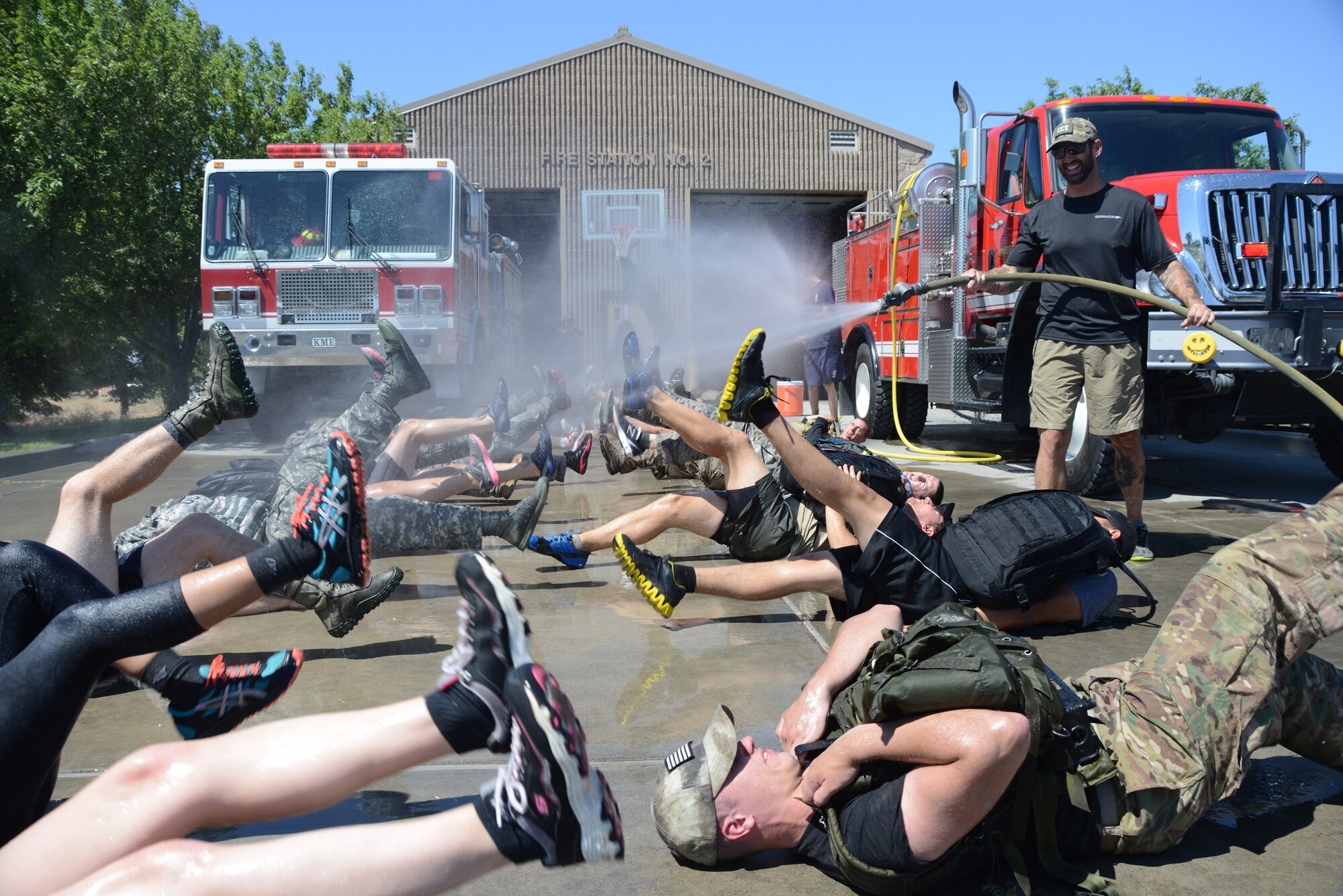 Mike Stewart, GORUCK cadre member, sprays participants of the GORUCK Light Challenge with water from a fire hose July 12, 2014, at Mountain Home Air Force Base, Idaho. The only relief participants had from scorching 90 degree heat of the July sun was from being blasted by fire hoses while performing flutter kicks on the pavement. (U.S. Air Force photo by Senior Airman Benjamin Sutton/Released)