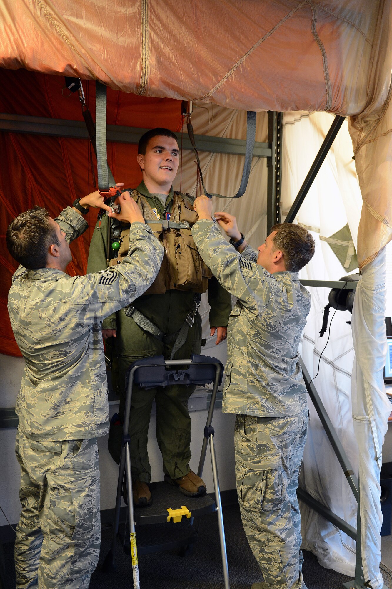 Tech. Sgt. Logan Davis (left), 62nd Operations Support Squadron survival, evasion, resistance and escape specialist, and Staff. Sgt. Kevin Randall (far right), 62nd OSS SERE specialist, strap Jerry Connolly, pilot for a day, into a parachuting simulator July 14, 2014, at Joint Base Lewis McChord, Wash. Prior to simulating parachuting, Connolly was given instructions on parachuting safety. (U. S. Air Force photo/Airman 1st Class Jacob Jimenez)