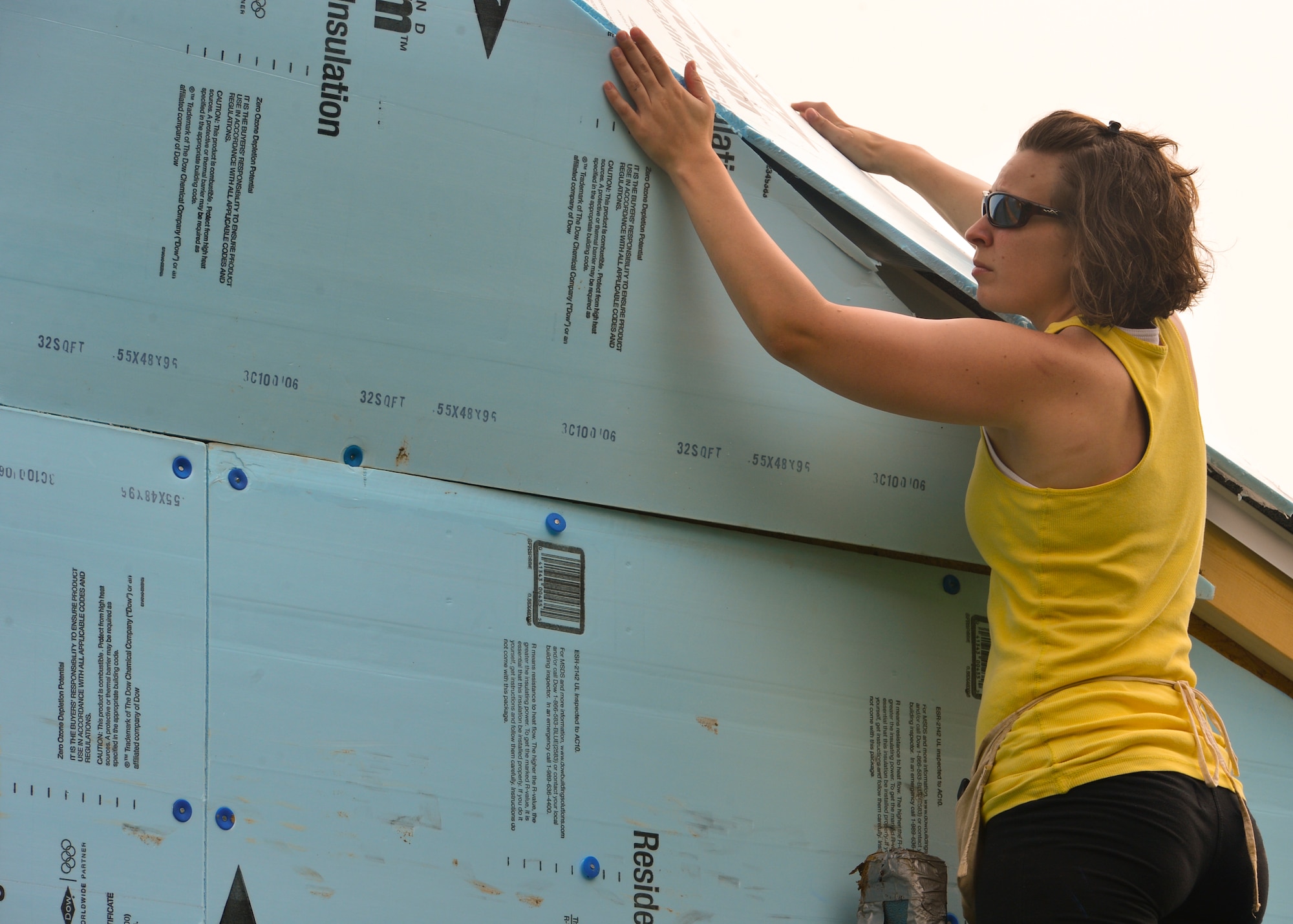 Jessica Stout, wife of Master Sgt. Jeffrey Stout, 436th Maintenance Squadron isochronal maintenance dock chief, stands on a ladder as she cuts residential sheathing insulation with an utility knife July 12, 2014, at a Habitat for Humanity construction site in Frederica, Del. Several family members of Airmen also volunteered at the event. (U.S. Air Force photo/Airman 1st Class Zachary Cacicia)	
