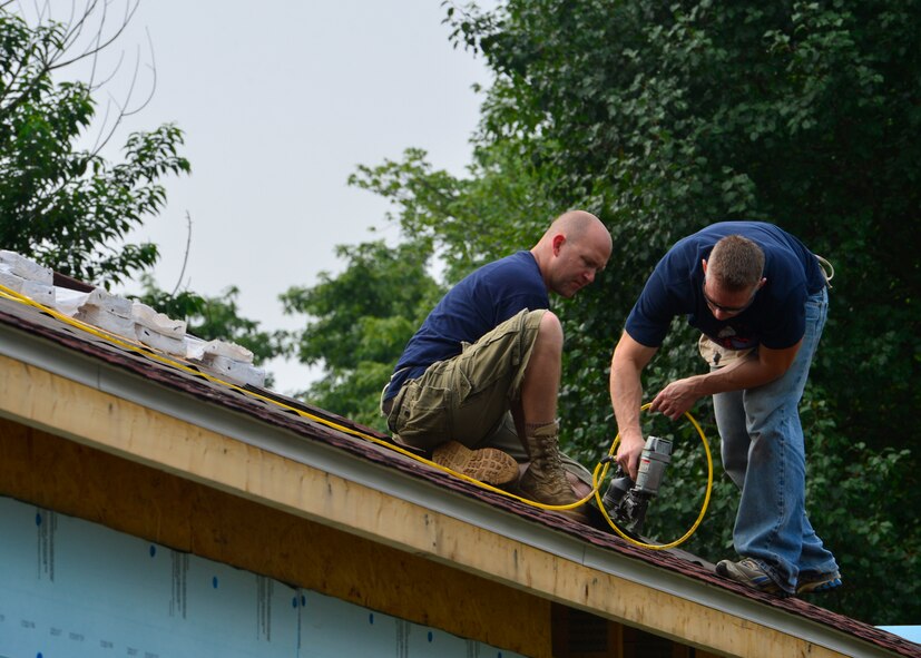 Tech. Sgt. Ray Dezur, 436th Aircraft Maintenance Squadron, left, and Master Sgt. Jeffrey Stout, 436th Maintenance Squadron isochronal maintenance dock chief, use a nail gun to attach roofing shingles July 12, 2014, at a Habitat for Humanity construction site in Frederica, Del. Nail guns were used to make the process faster. (U.S. Air Force photo/Airman 1st Class Zachary Cacicia)	