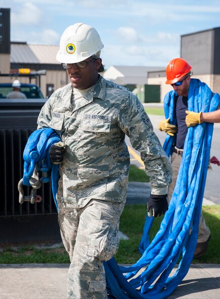 U.S. Air Force Airman 1st Class Justin Mclendon, 23d Civil Engineer Squadron heating, ventilation and air conditioning journeyman, carries lifting straps before removing an air-conditioning unit at Moody Air Force Base, Ga., July 14, 2014. Airmen secured the straps to the bottom of the unit so they could use a crane to lift and remove it. (U.S. Air Force photo by Senior Airman Jarrod Grammel/Released) 
