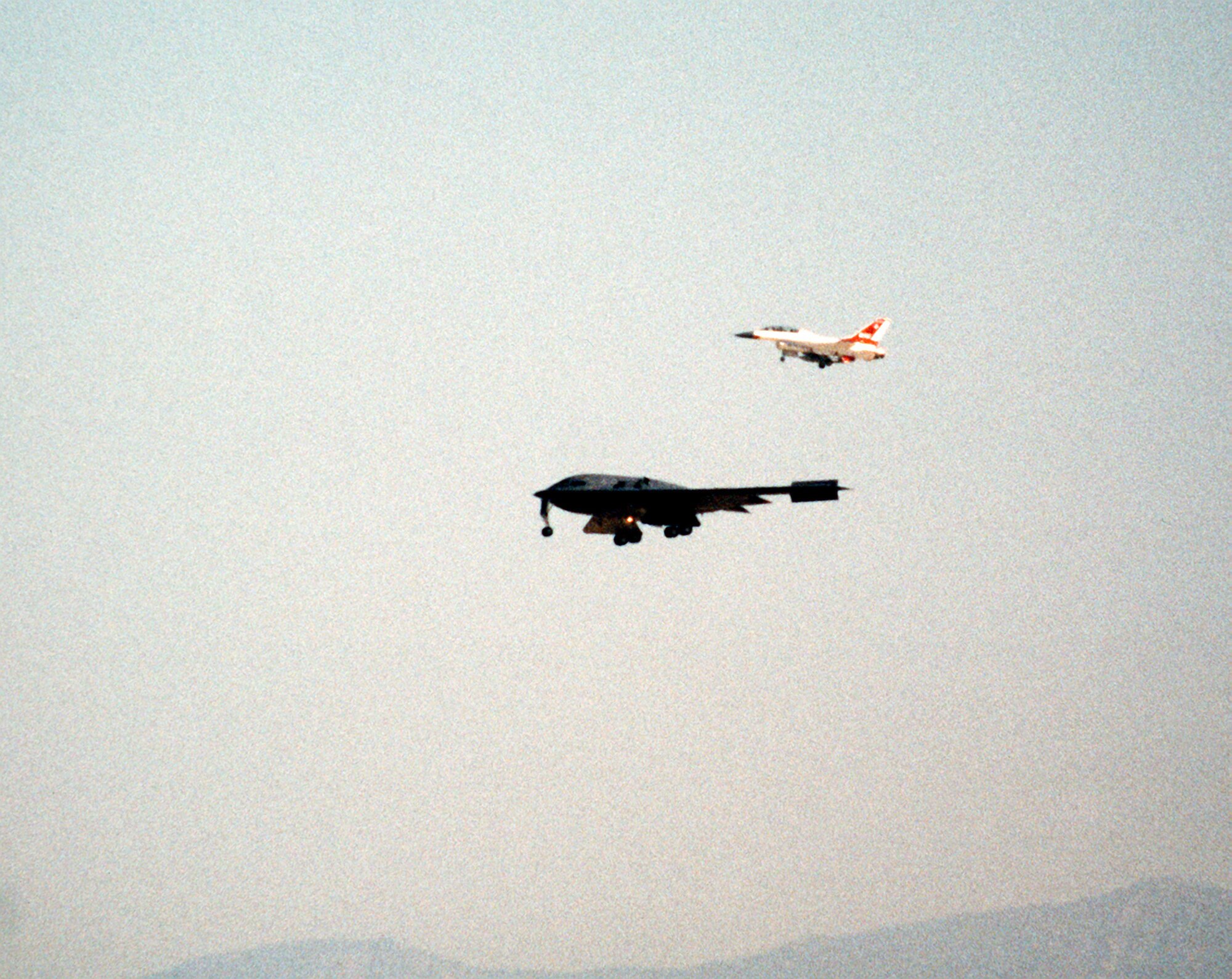 An F-16B Fighting Falcon accompanies the first ever B-2 Spirit to take flight July 17, 1989, over California. The flight took place from the Northrop Grumman production facility in Palmdale, California to Edwards Air Force Base, California where the B-2 would remain in the testing phase until 1993, when the first operational aircraft was delivered to Whiteman AFB, Missouri. (Defense Imagery Management Operations Center photo/Released)