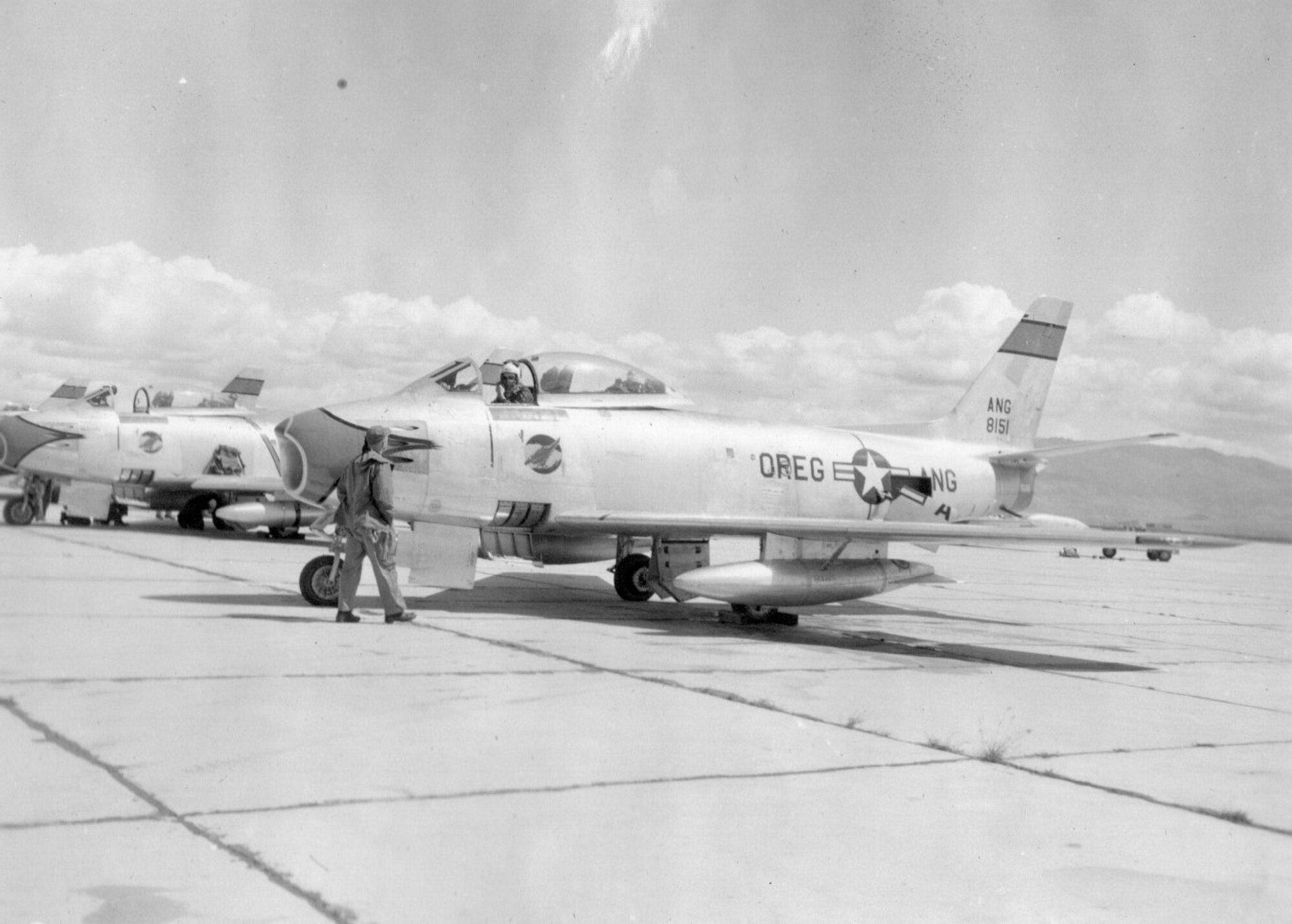 A fighter pilot prepares for a sortie in an OreANG F-86A Sabre jet fighter, serial number 48-151, of the 123nd Fighter-Interceptor Squadron during annual training at Gowen Field, Idaho, June 18,1954.  Note the distinctive Redhawk emblem on the fuselage below the cockpit.  The nose flash and stripe on the tail are colored green with black trim. (Courtesy 142FW History Archives)