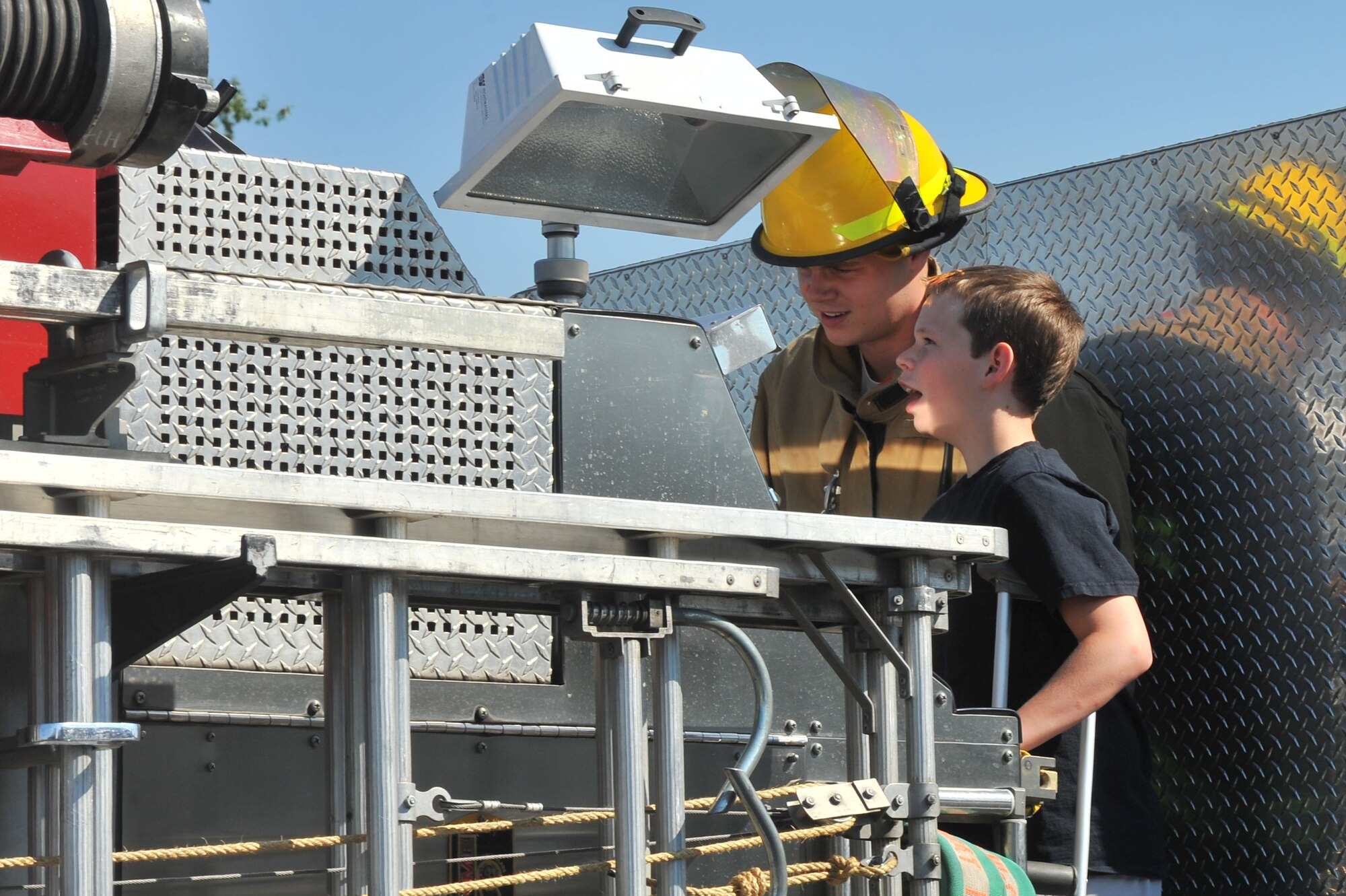 Airman 1st Class Dakota Pellegrini teaches Zayne Rutter how to spray water from a fire truck while Zayne was 'Airman for a Day' July 11, 2014, at Fairchild Air Force Base, Washington. Airman for a Day is a program that allows children to come out to the base and experience what it is like to be a member of the Air Force. Pellegrini is a 92nd Civil Engineer Squadron fire fighter. (U.S. Air Force photo by Staff Sgt. Veronica Montes/Released)