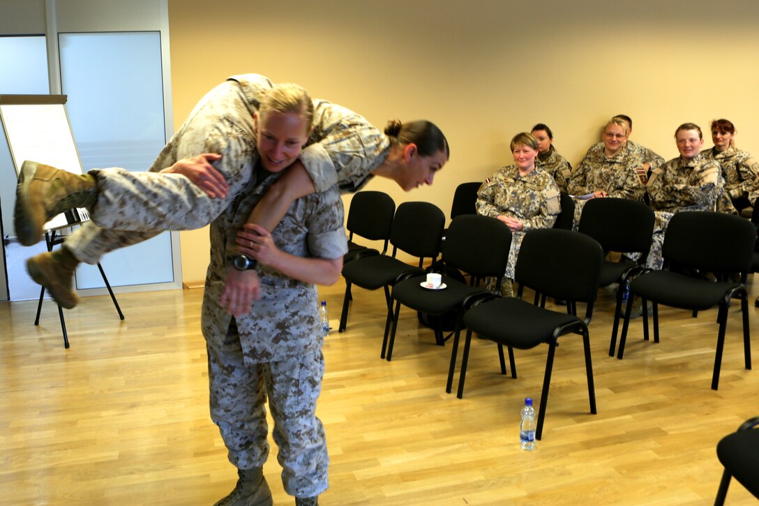 During a knowledge exchange of physical fitness test requirements for females between the U.S. Marine Corps and the Latvian Armed Forces, Capt. Claire E. Henry demonstrates the “fire-man’s carry” portion of the Combat Fitness Test with Gunnery Sgt. Tiffany C. Hudgins. U.S. Marines introduced Female Engagement Team concepts to a group of Latvian servicemembers from June 17-19 at Adazi Military Base, Latvia; this introduction was the first step for the Baltic partner to further evaluate the capability for use within their own military.