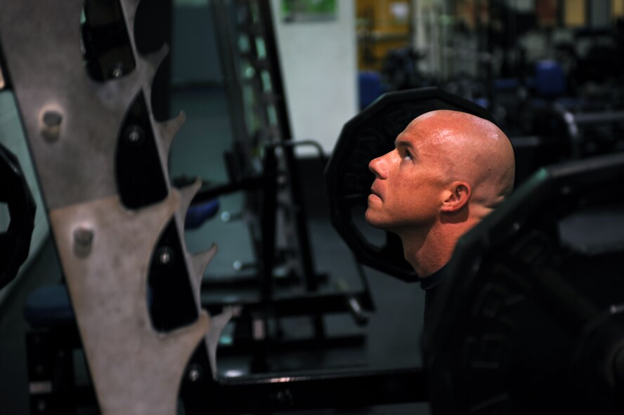 U.S. Air Force Senior Airman Seth Michael, 7th Equipment Maintenance Squadron, performs squats during his workout in the fitness center July 16, 2014, on Dyess Air Force Base, Texas. Michael uses his lunch breaks to complete workouts that include lifting weights and running; about 60 miles a week. (U.S. Air Force photo by Senior Airman Shannon Hall/Released)