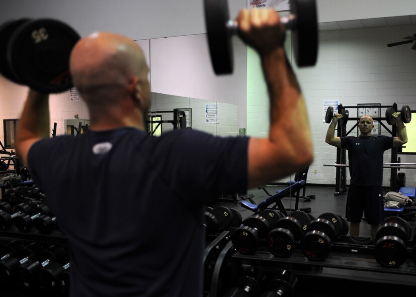 U.S. Air Force Senior Airman Seth Michael, 7th Equipment Maintenance Squadron, performs shoulder presses with 35 pound dumbbells in the fitness center July 16, 2014, on Dyess Air Force Base, Texas. As part of his commitment and training, in preparation for the 2014 Air Force Marathon, Michael maintains a healthy diet and works out twice a day, seven days a week. (U.S. Air Force photo by Senior Airman Shannon Hall/Released)