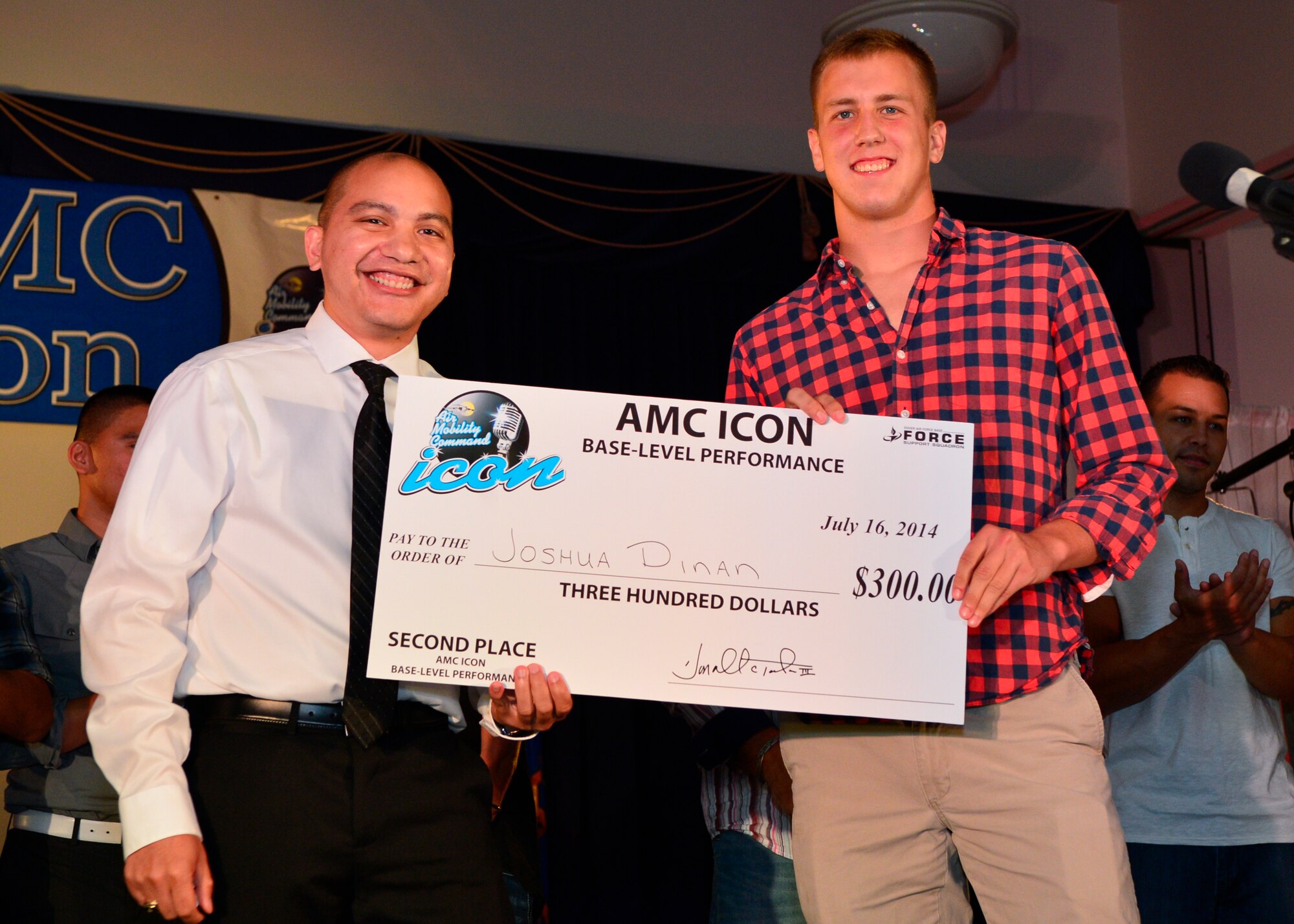 First Lt. Christopher Trejo, 436th Force Support Squadron civilian personnel section, left, presents Airman 1st Class Joshua Dinan, 436th Aircraft Maintenance Squadron, with a giant check for $300 July 16, 2014 at the Landings Club on Dover Air Force Base, Del. The $300 was the second place award for the Air Mobility Command Icon competition at DAFB. (U.S. Air Force photo/Airman 1st Class Zachary Cacicia)