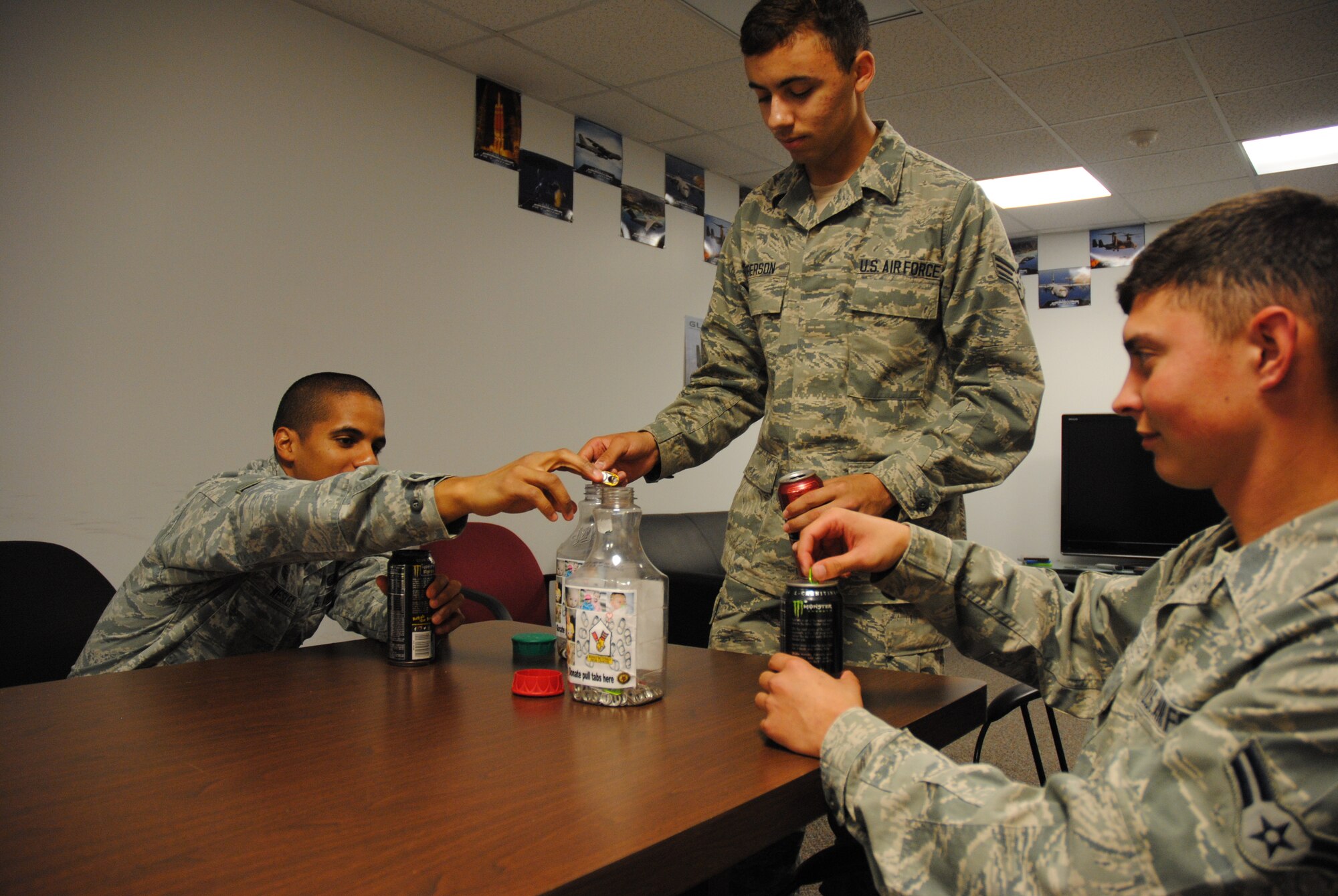 Members of the Grand Forks Air Force Base Honor Guard drop pop tabs into collection containers located inside the Base Honor Guard break room on July 14, 2014. The organization of approximately a dozen active-duty members from Grand Forks AFB, N.D., continues to collect pop tabs after contributing more than 1,100 of the tiny aluminum pieces to Air Force Sergeants Association, Chapter 964,which along with American Legion Post #6 in Grand Forks, N.D., donated a grand total of 68,003 pop tabs to the Ronald McDonald House in Bismarck, N.D. (U.S. Air Force photo/Staff Sgt. Luis Loza Gutierrez) 
