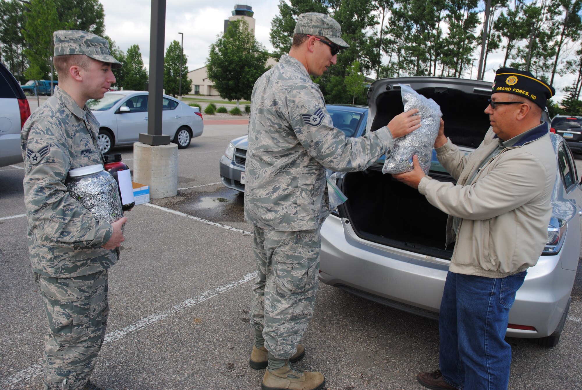 (From left) Senior Airman Michael Murphy and Staff Sgt. Thomas Spencer from the 69th Reconnaissance Group hand bags and plastic containers filled with soda pop tabs to Robert Greene, American Legion Post #6 commander, on June 25, 2014.  Greene took the pop tabs to the American Legion Department of North Dakota Convention in Minot where officials confirmed that 68,003 pop tabs were collected for the Ronald McDonald House in Bismarck, N.D. (U.S. Air Force photo/Staff Sgt. Luis Loza Gutierrez) 
