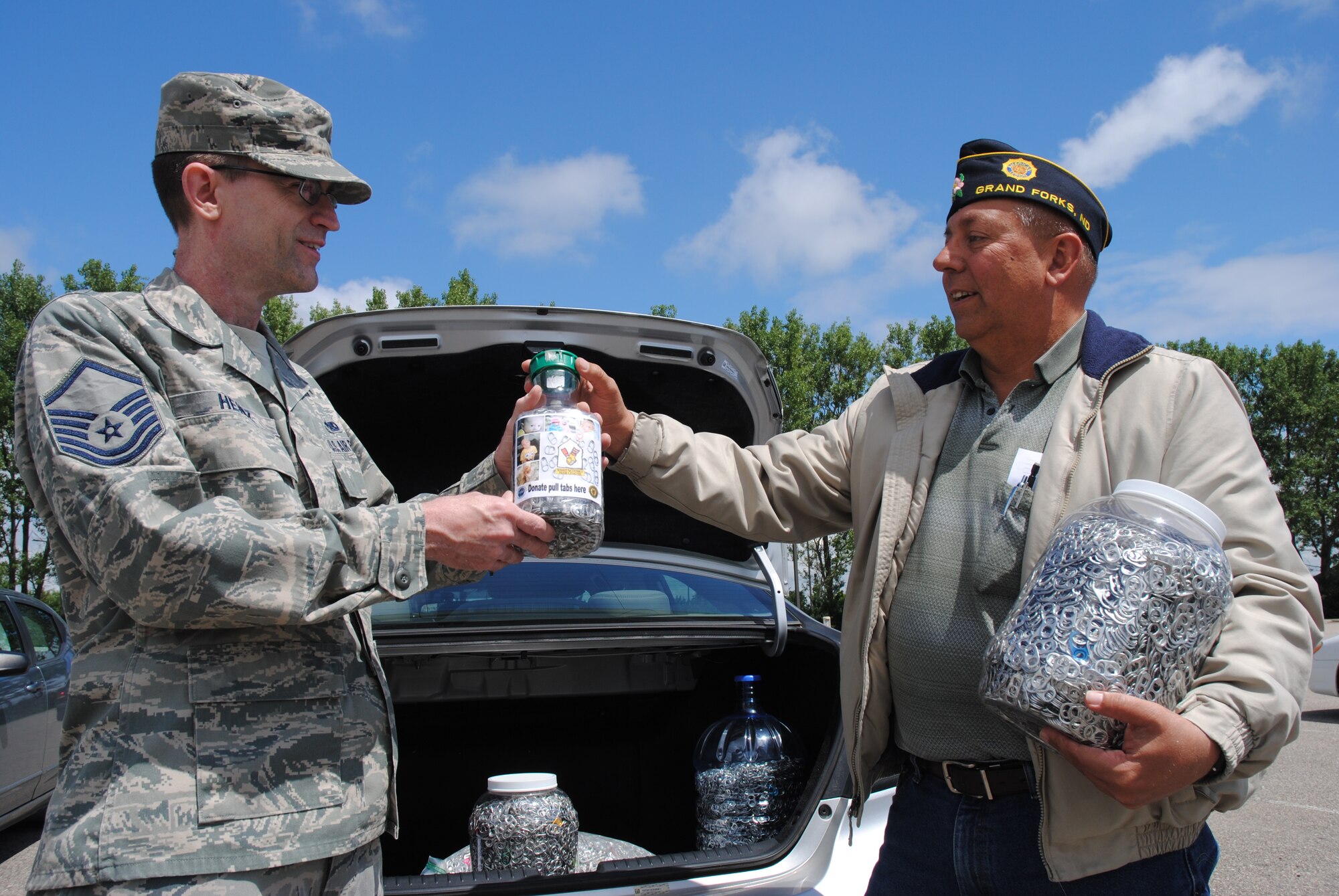 (From left) Master Sgt. Russell Heinz, Air Force Staff Sergeants Association, Chapter 964 project coordinator, hands another container filled with soda pop tabs to Robert Greene, American Legion Post #6 commander, June 25, 2014, on Grand Forks Air Force Base, N.D. The two gentlemen led a joint effort between their organizations to collect as many soda pop tabs for the Ronald McDonald House in Bismarck, N.D. The Legionnaires from the city of Grand Forks, N.D. and the Warriors of the North collected more than 68,000 pop tabs. (U.S. Air Force photo/Staff Sgt. Luis Loza Gutierrez) 
