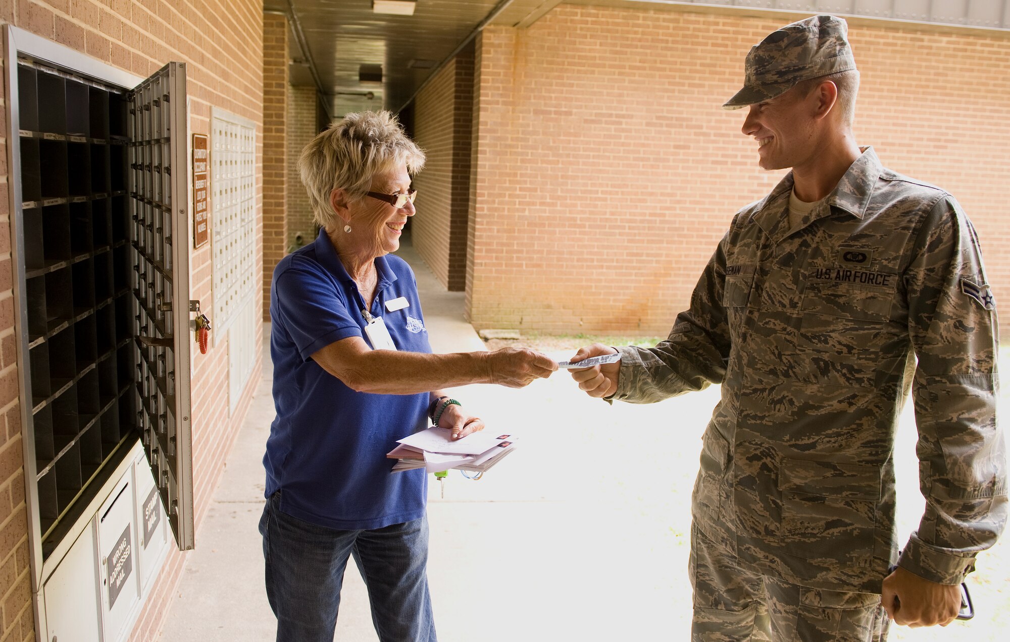 Patty Armstrong, Postal Service Center mail clerk, hands Airman 1st Class Roman Huseman a blue slip while delivering mail to the dormitories on Hurlburt Field, Fla., July 16, 2014. Blue slips serve as tickets for Airmen, notifying them that their packages are awaiting pickup. (U.S. Air Force photo/Senior Airman Kentavist P. Brackin)