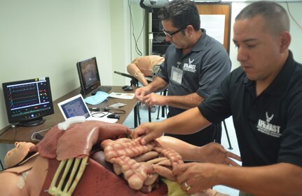 David Torres, Air Force Medical Modeling and Simulation Training Operations Department, Air Education and Training Command, Joint Base San Antonio-Randolph and Tony Garcia, Simulation Operator, Medical Research Training Center, Camp Bullis, Texas, places synthetic organs into the Tactical Combat Casualty Care Cut Suit. The organs can be anatomically placed. The computer monitors in the background control blood flow and other important vitals.