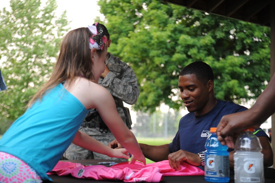 DeShawn Shead signs autographs during the 'Heros of 12’ Military Appreciation Tour at Fairchild Air Force Base, Washington, July 17, 2014. The tour consists of Seahawk players, Seagals cheerleaders, the Blue Thunder Band, Taima the Hawk with falconer David Knutson, Blitz the official team mascot and the Lomabardi trophy. Shead plays defensive back. (U.S. Air Force photo/Airman 1st Class Janelle Patiño)