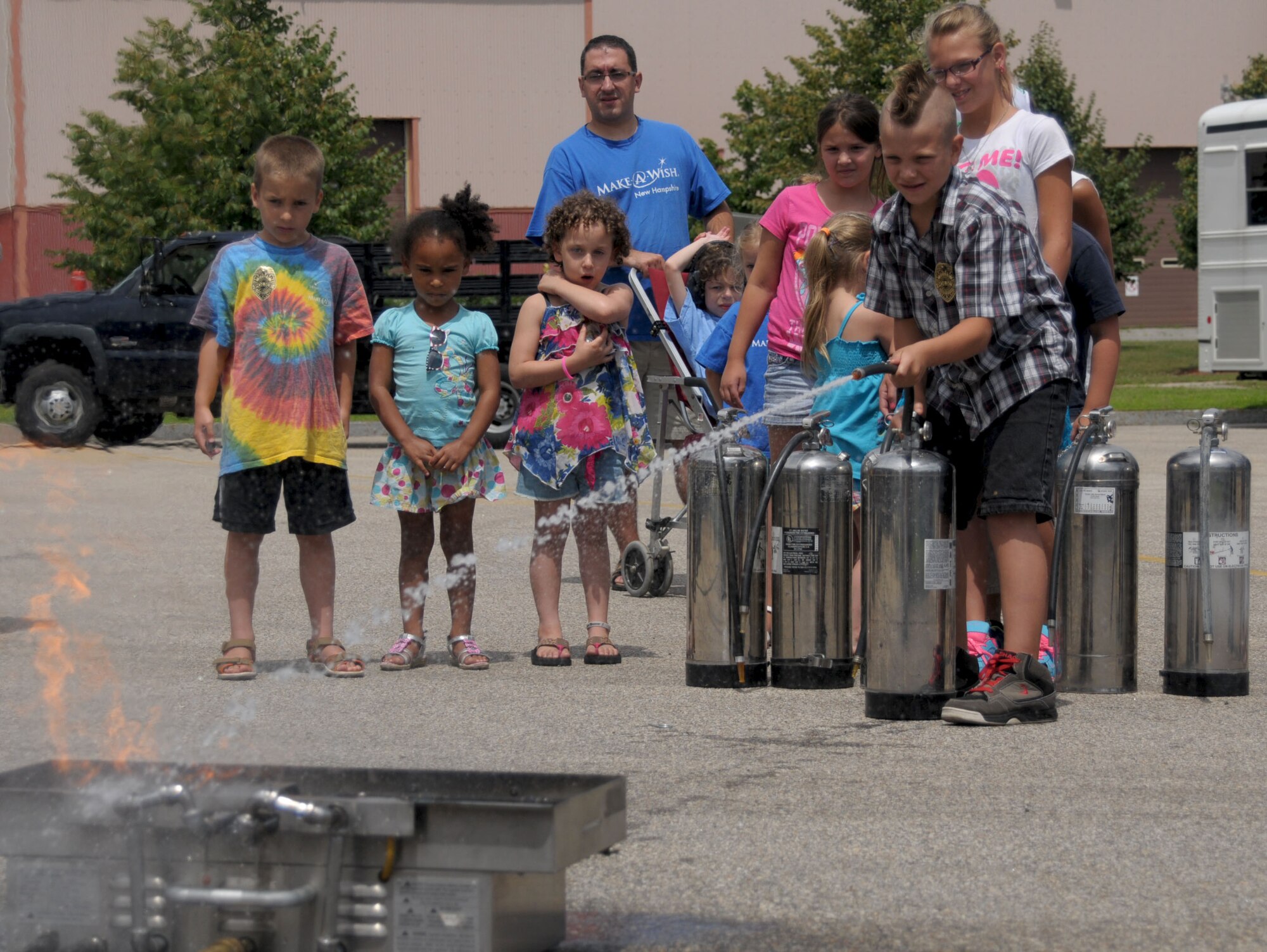 PEASE AIR NATIONAL GUARD BASE, N.H. – Children from the Make-A-Wish Foundation take turns putting out a controlled fire outside the Fire Department during a demonstration presented by firefighters here July 17. Eight children and their families were welcomed to Pease by Airmen who lined the sidewalk at the main gate, received demonstrations from the Dover Mounted Patrol and a Military Working Dog demonstration, enjoyed lunch at the Fire Department and toured the inside of a KC-135. (N.H. Air National Guard photo by Airman 1st Class Kayla McWalter/RELEASED)