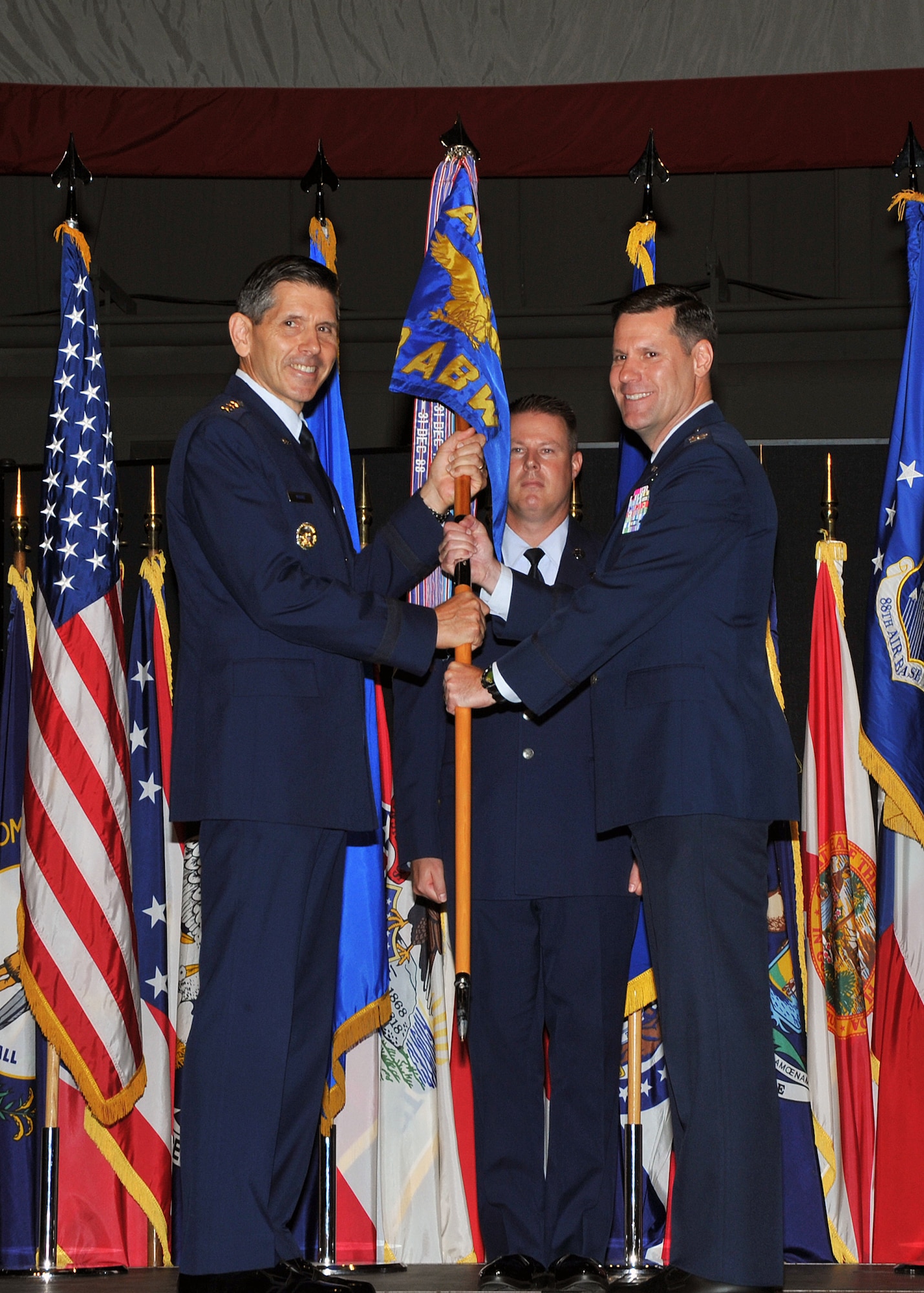 Lt. Gen. C.D. Moore II, Air Force Life Cycle Management commander (left), passes the guidon to Col. John Devillier (right) during the 88th Air Base Wing change of command ceremony. The event took place at the National Museum of the U.S. Air Force July 17. Chief Master Sergeant Charles Hoffman, 88 ABW command chief (background), represents the base's enlisted Airmen. (Air Force photo by Mike Libecap)