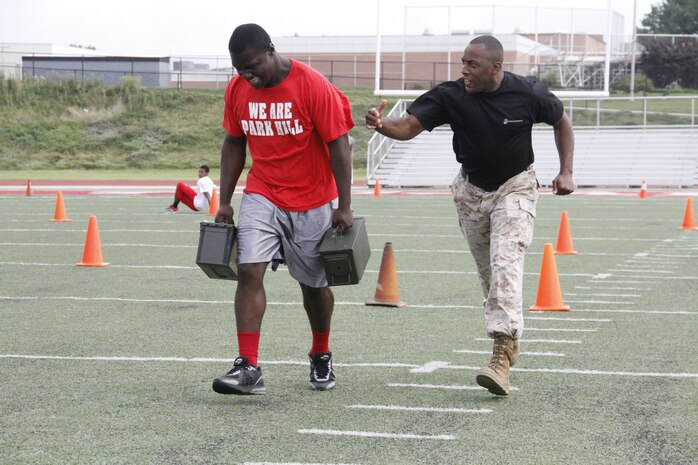 Desmond A. Stirgus, a Park Hill High School Trojans junior nose tackle, receives motivation from Sgt. Maj. Johnnie M. Hughes, Recruiting Station Kansas City sergeant major, as he carries two 30-pound ammunition cans during the maneuver-under-fire portion of the Combat Fitness Test at the Trojans' football field July 17, 2014. Players from both the Trojan football and volleyball teams took part in the CFT. 