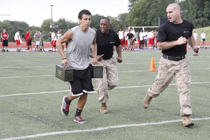 Sergeant Major Johnnie M. Hughes, Recruiting Station Kansas City sergeant major, and Sgt. Kyle F. Woodworth, a RS Kansas City, Recruiting Sub-Station Gladstone recruiter, encourage sophomore Ciaron S. Willis, a Park Hill High School Trojans wide receiver and defensive back, as he carries two 30-pound ammunition cans during the maneuver-under-fire portion of the Combat Fitness Test at the Trojans' football field July 17, 2014. 