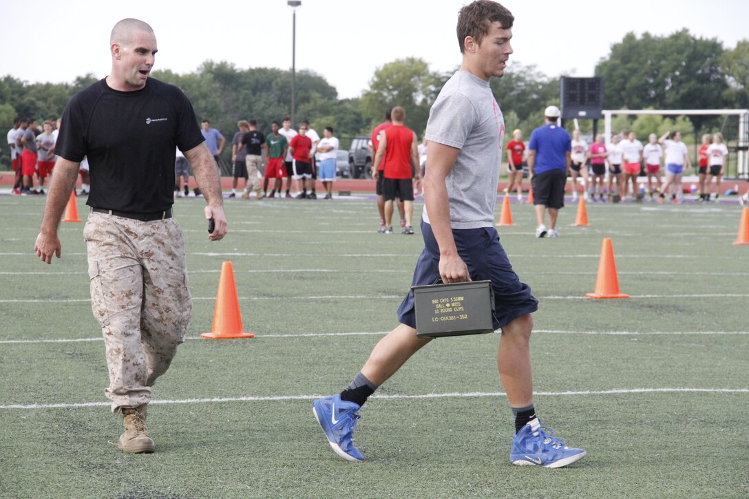 Sergeant Kyle F. Woodworth, a Recruiting Station Kansas City, Recruiting Sub-Station recruiter, encourages junior Aiden S. Byrd, a Park Hill High School Trojans free safety, during the maneuver-under-fire portion of the Marine Corps' Combat Fitness Test at the Trojans' football field July 17, 2014. Players from both the Trojan football and volleyball teams took part in the CFT. The CFT consists of an 880-meter sprint, 30-pound ammo-can lifts in two minutes, and the maneuver-under-fire. 