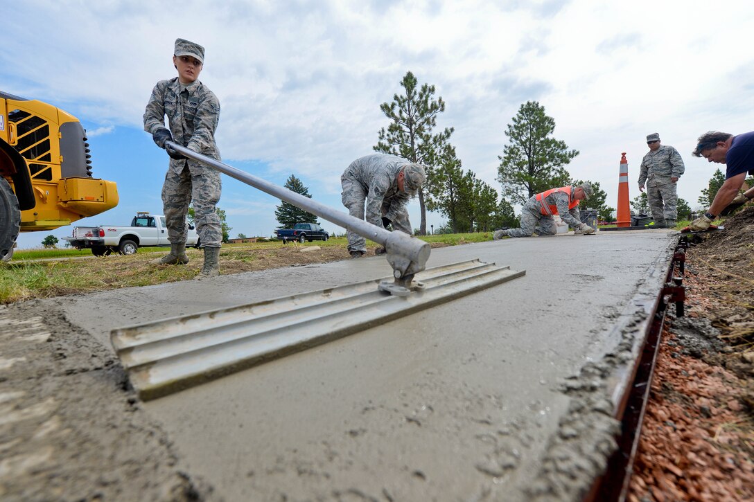 Airman 1st Class Kattie Schurman, 28th Civil Engineer Squadron heavy equipment and pavement technician, evens out the surface of a concrete pad at Ellsworth Air Force Base, S.D., July 16, 2014 to renovate base sidewalks. Heavy equipment and pavement technicians are required to inspect each road, sidewalk and parking lot for structural integrity and damage after the winter season. (U.S. Air Force photo by Senior Airman Zachary Hada/Released)