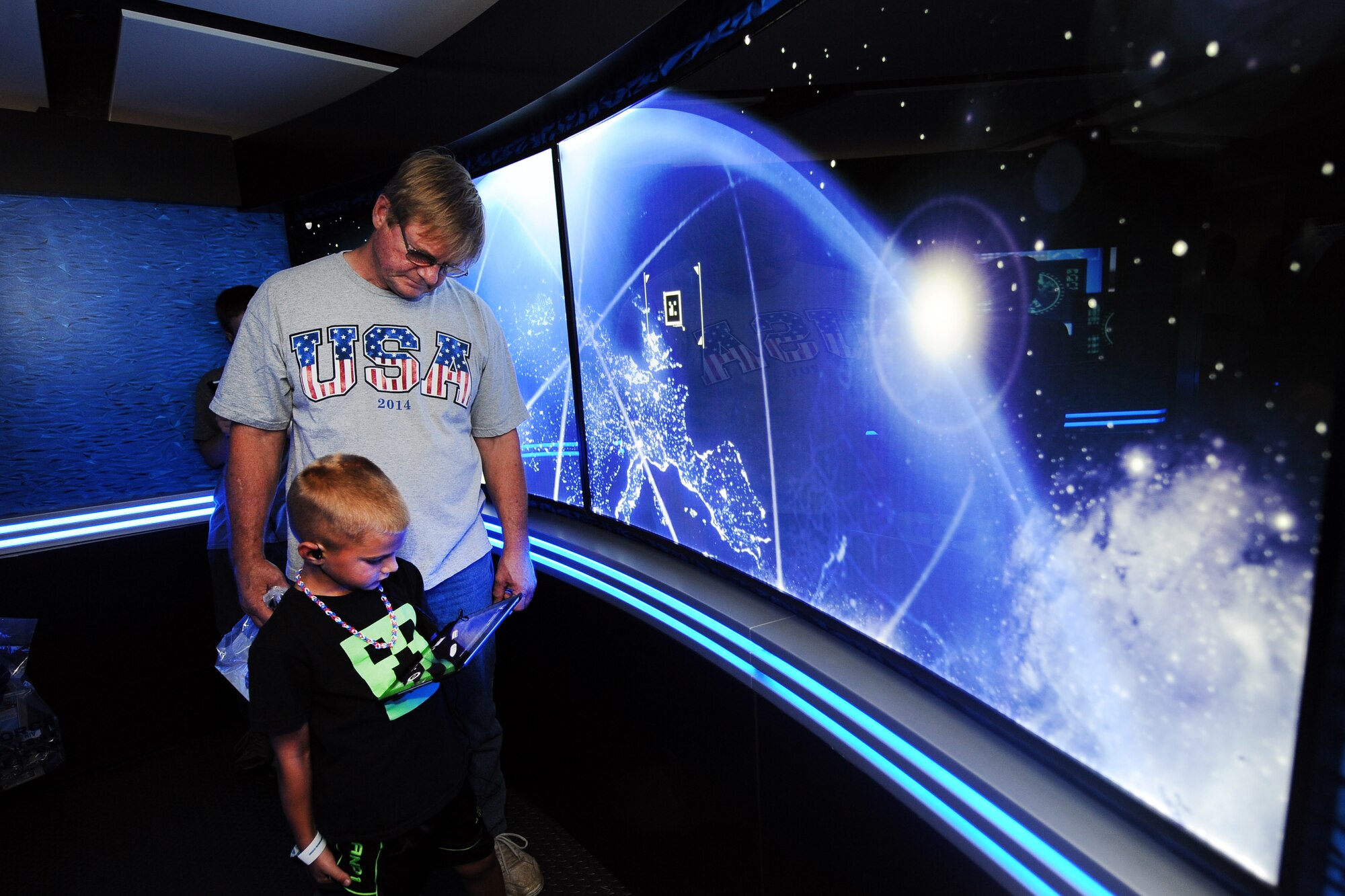 Seven-year-old Teagan Zeringue, alongside his grandfather Jim Schneider, walk through a high-tech U.S. Air Force Command Center Alpha exhibit while attending the 2014 Defenders of Freedom Open House and Air Show at Offutt Air Force Base, Nebraska July 19.  The Command Center Alpha exhibit took people on and interactive tour through three distinct modules.  The hand held tablets interacted with the wall around them.  (U.S. Air Force photo by Josh Plueger/Released)
