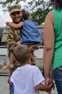 U.S. Army Sgt. Raphael Fernandez, 612th Movement Control Team, 53rd Transportation Battalion, 7th Transportation Brigade (Expeditionary), speaks to son while carrying his daughter during a deployment ceremony at Fort Eustis, Va., July 19, 2014. The team deployed to Afghanistan in support of Operation Enduring Freedom. (U.S. Army photo by Spc. Marian Alleva/Released)