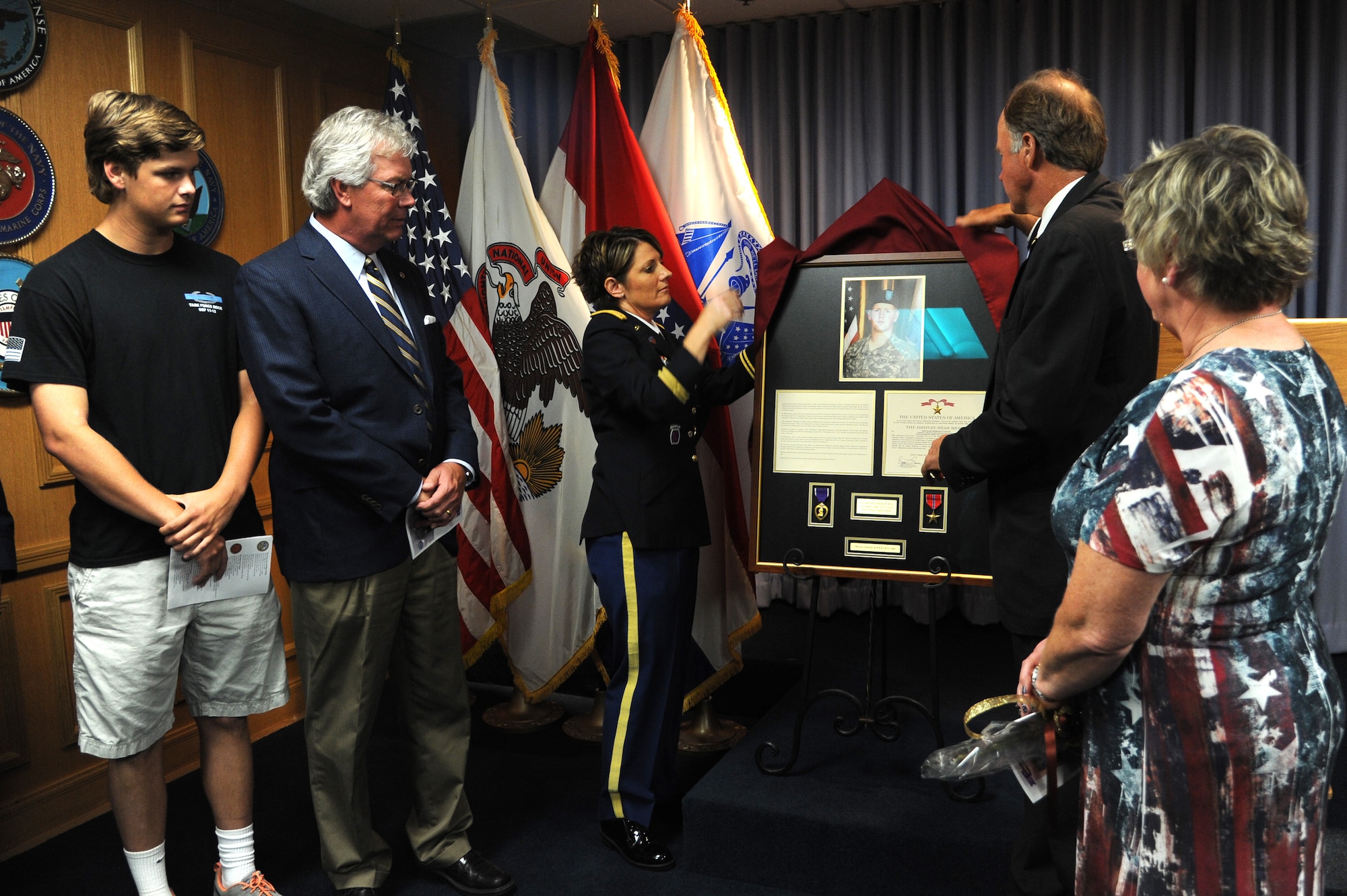 Bob McDavid, the Mayor of Columbia, MO, and Lt. Col. Patricia George, St. Louis Military Entrance Processing Station and 11th Battalion commander unviel a frame containing a photo of U.S Army Specialist Sterling Wyatt, his purple heart, Bronze Star and his biography during a dedication ceremony at the St. Louis MEPS in St. Louis, MO, July 17, 2014. Sterling was killed in action when his vehicle was attacked with an enemy improvised explosive device while on patrol in Kandahar Province Afghanistan July 11, 2011. (U.S. Air Force photo/Senior Airman Tristin English)