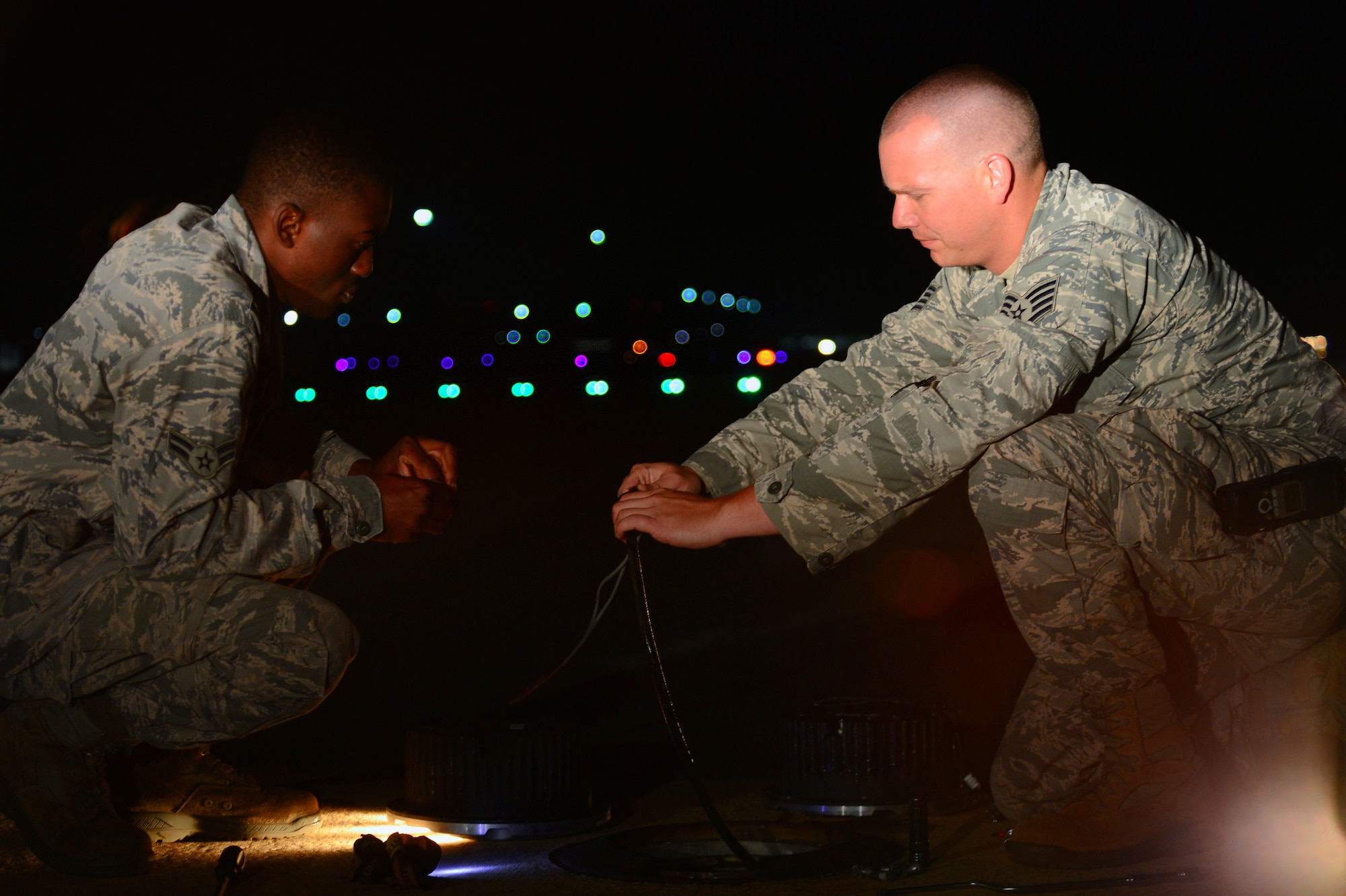 U.S. Air Force Airman 1st Class Ernest Kuma, 20th Civil Engineer Squadron electrical systems journeyman and Staff Sgt. Nicholes Crumb, 20th CES electrical systems craftsman, install a new approach light on the runway at Shaw Air Force Base, S.C., July 16, 2014. More than 20 rows of five lights line the ends of the runway, ensuring pilots know where the start of the runway is. (U.S. Air Force photo by Airman 1st Class Jensen Stidham/Released)