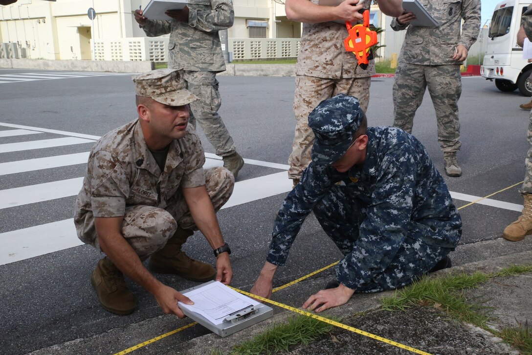 Gunnery Sgt. Antonio Lopez, left, demonstrates proper military police roadway measuring technique alongside Petty Officer 3rd Class Andrew Dowling July 14 at Camp Foster as part of the Traffic Collision Investigation Course. The day of practical application training took the service members out of the classroom and onto the streets. The hands-on training familiarized the service members with what to look for when at the scene of an accident. Lopez is a Calipatria, California, native and an accident investigator with the Marine Detachment at Lackland Air Base, Training Command, Training and Education Command. Dowling is a master-at-arms 3 with Commander Fleet Activities Okinawa Security. (U.S. Marine Corps photo by Lance Cpl. Wes J. Lucko/Released)