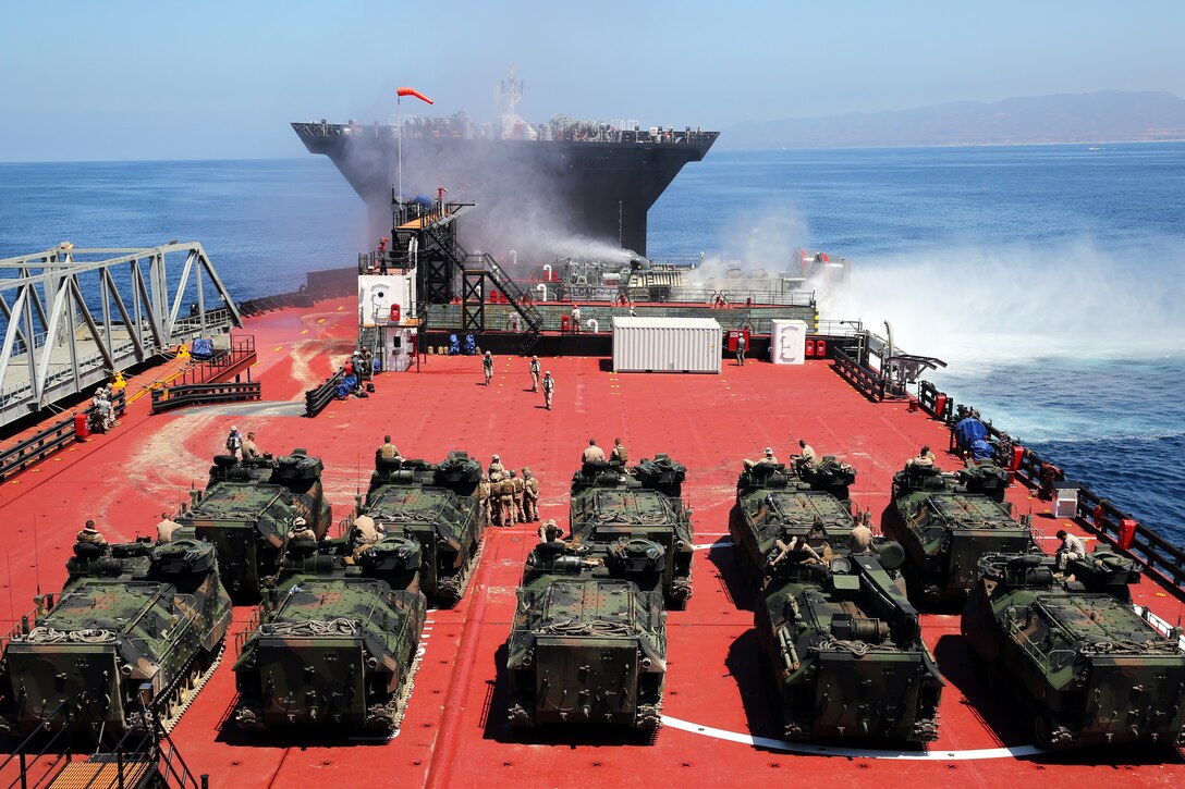 Amphibious assault vehicles with 3rd Assault Amphibian Battalion, 1st Marine Division, line the deck of the USNS Montford Point, a Mobile Landing Platform, as a Landing Craft Air Cushion with Assault Craft Unit 5, offloads more AAVs onto the vessel during the testing of a seabasing capability, July 9, 2014. The MLP is a new type of Maritime Pre-Positioning Ship that facilitates the transfer of military equipment and personnel from large ships to small landing craft. 