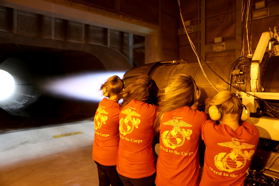 Spouses with Marine Aircraft Group (MAG) 11 stand next to an F-18 Hornet jet engine in full afterburner during a jet engine test cell demonstration during a Jane Wayne Day aboard Marine Corps Air Station Miramar, Calif., July 19. The family members also conducted the obstacle course and a combat fitness test. 