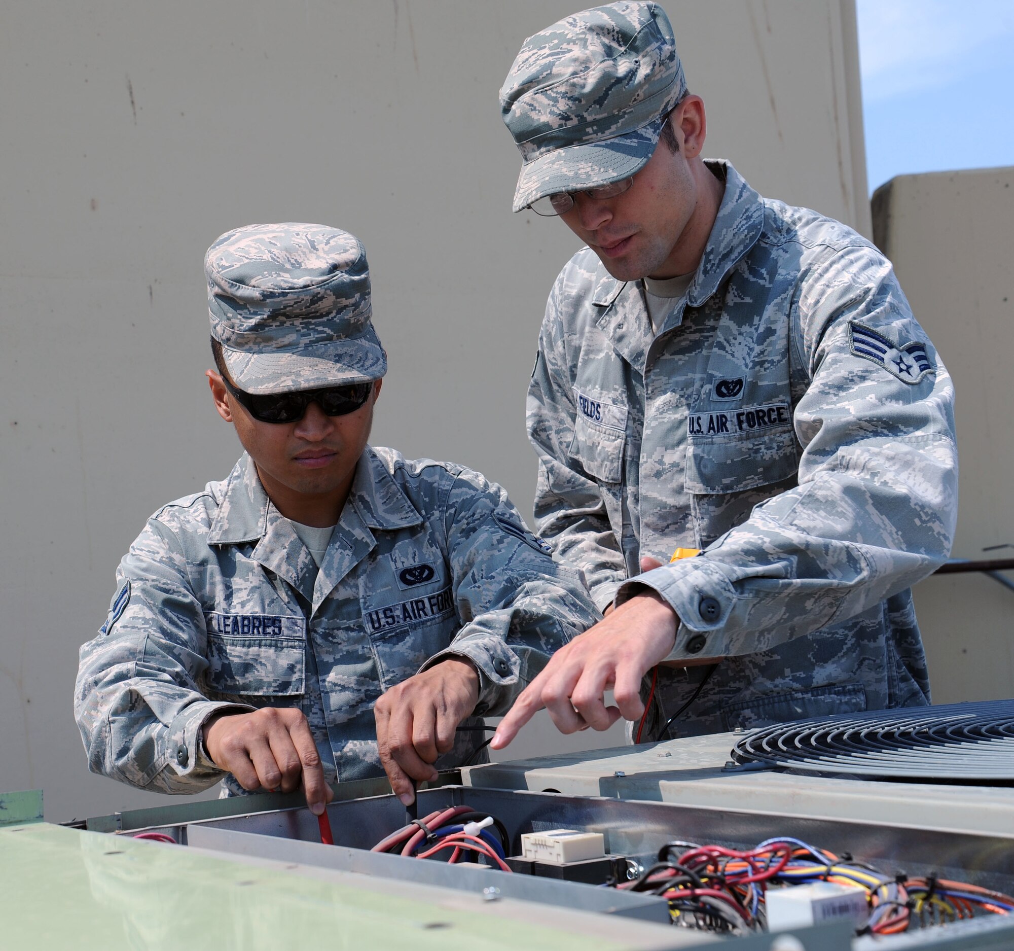 Airman 1st Class Josh Leabres ohms out a unit while checking for continuity between wires of an air conditioning unit, while Senior Airman William Fields supervises at Fairchild Air Force Base, Washington on July 21, 2014.  As a heating, ventilation and air conditioning journeymen, Leabres and Field daily work is mostly consumed with preventative maintenance on infrastructure equipment throughout the base. These 92nd CE Airmen are responsible for keeping all air conditioning systems running, heating, cooling, refrigeration and some domestic water heaters in working condition.  (U.S. Air Force photo by Staff Sgt. Samantha Krolikowski/Released)