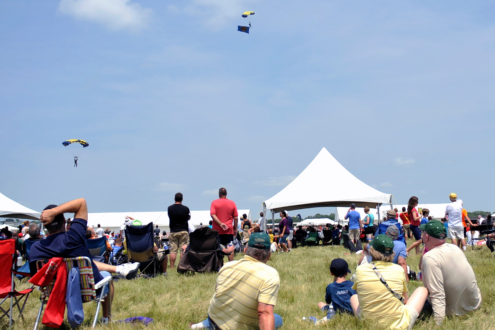 Air show patrons sit in the grass and watch as the U.S. Navy Leap Frogs parachute demonstration team comes in for a landing at the 2014 Defenders of Freedom Open House and Air Show July 19 at Offutt Air Force Base, Nebraska.  The Leap Frogs represent Naval Special Warfare and the U.S. Navy.  The members of this team must be military freefall qualified, be serving on at least their second enlistment, have completed at least two operational deployments and be recommended by their chain of command.  (U.S. Air Force photo by Jeff W. Gates/Released)