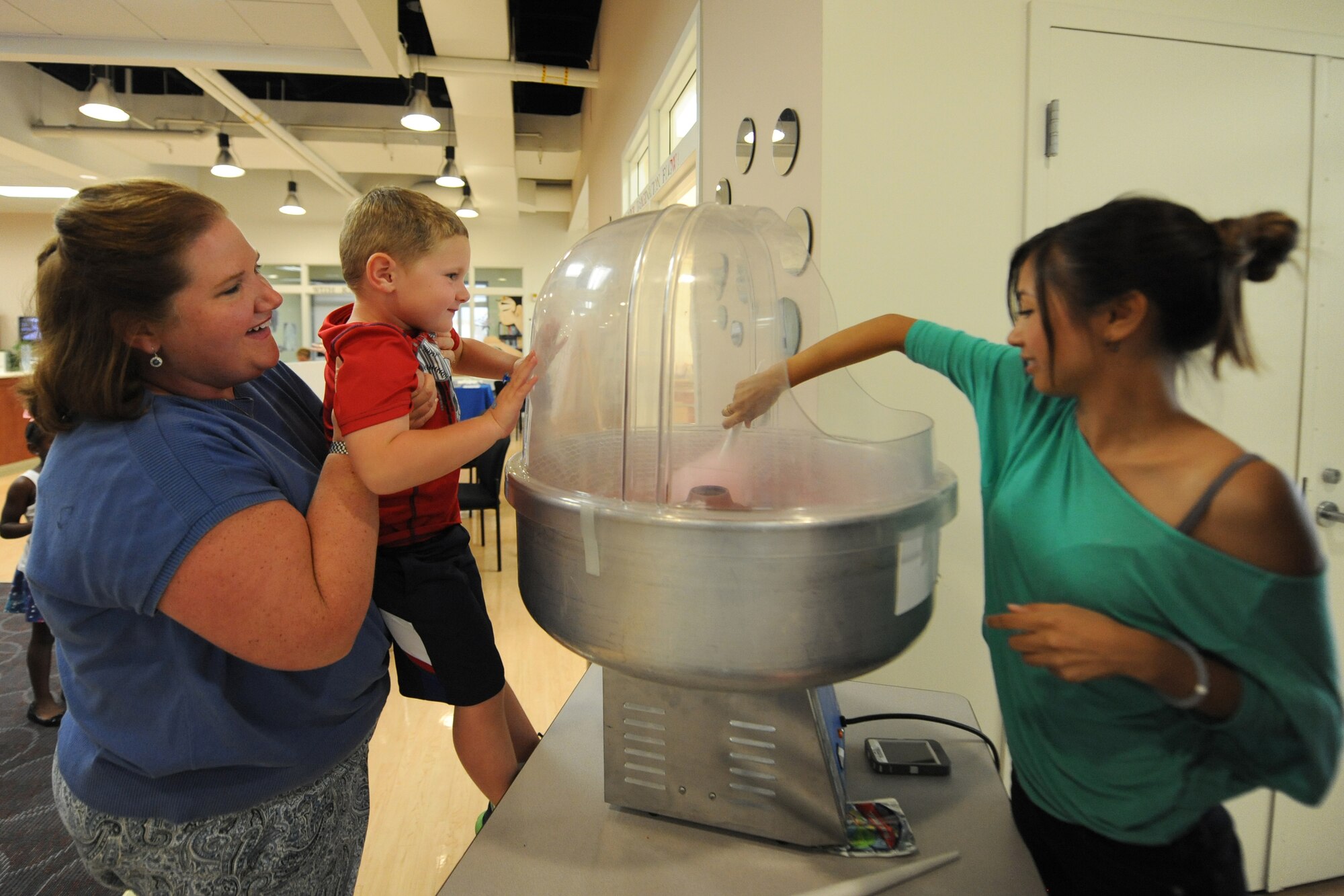 Kristin Moore, wife of Col. Rick Moore, 436th Airlift Wing commander, holds their son Mitchell up to see how cotton candy is made during a deployed families dinner at the Youth Center July 17, 2014 at Dover Air Force Base, Del. Janella Tauchus, daughter of Chief Master Sgt. Dennis Tauchus, 736th Aircraft Maintenance Squadron, volunteered to make cotton candy at the event. (U.S. Air Force photo/Staff Sgt. Elizabeth Morris)