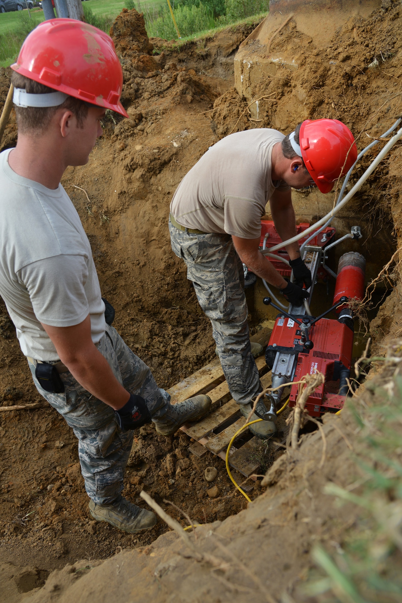 U.S. Air Force Staff Sgt. Steven Land tightens a water hose connection as Staff Sgt. Andrew Goodrick watches at Langley Air Force Base, Va., July 22, 2014. The 820th Rapid Engineer Deployable Heavy Operational Repair Squadron Engineer electricians from Nellis Air Force Base, Nev., are trenching electric lines and installing pole foundations at Eagle Park. (U.S. Air Force photo by Senior Airman Aubrey White/Released) 