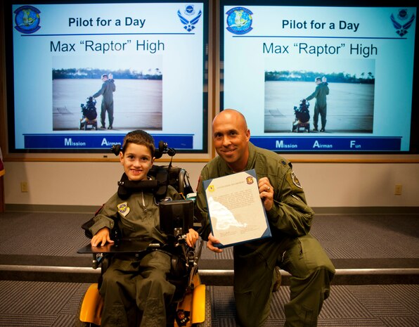 Lt. Col. Cassius Bentley, 15th Airlift Squadron commander, presents Max High, son of Capt. Aaron High, 15th AS pilot, with a certificate recognizing him as an honorary member of the squadron as part of the Pilot for a Day program July 15, 2014. The goal of the Pilot for a Day program is to provide children who have serious or chronic conditions and their families with the opportunity to be a guest of one of Joint Base Charleston’s squadrons for a day. Max also received a pilot’s jacket, scarf and pilot wings, co-piloted a C-17 simulator and toured a C-17. (Air Force photo by Staff Sgt. William A. O’Brien)