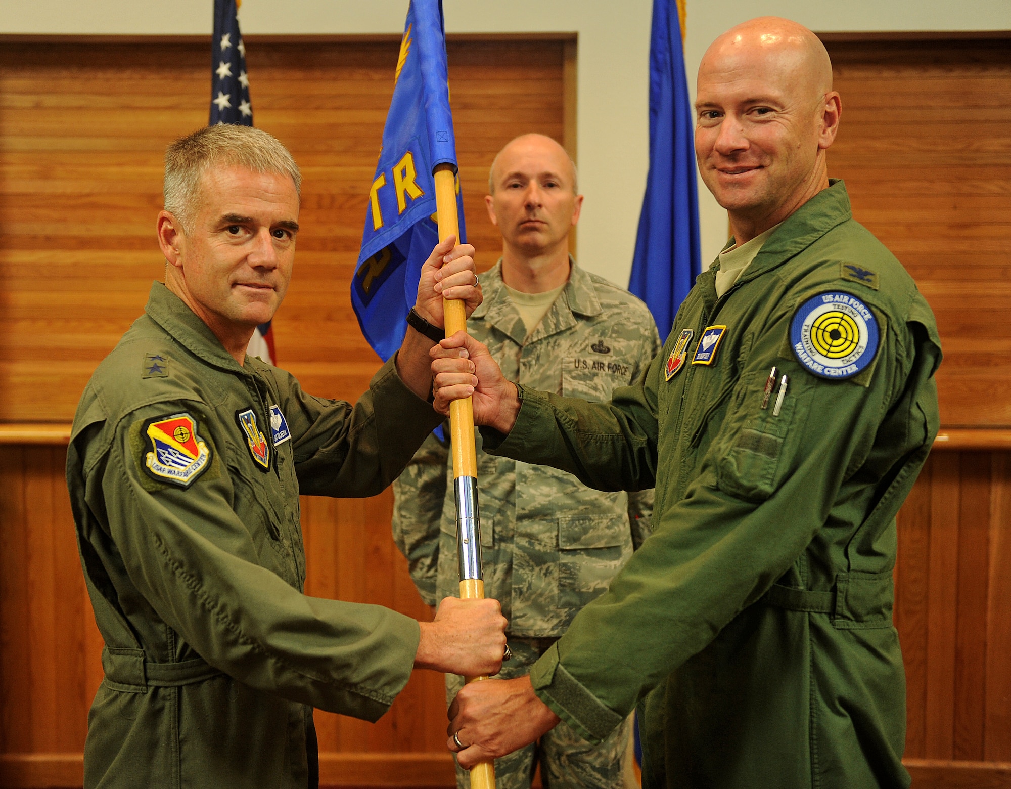 Maj. Gen. Jay Silveria, U.S. Air Force Warfare Center commander, passes the Nevada Test and Training Range guidon to the new NTTR commander, Col. Thomas E. Dempsey III, during a change of command ceremony at Nellis Air Force Base, Nev., July 18, 2014. Dempsey and the NTTR are responsible for providing a flexible, realistic and multidimensional battle-space for U.S. forces to conduct testing, training and tactics development. (U.S. Air Force photo by Staff Sgt. Siuta B. Ika)