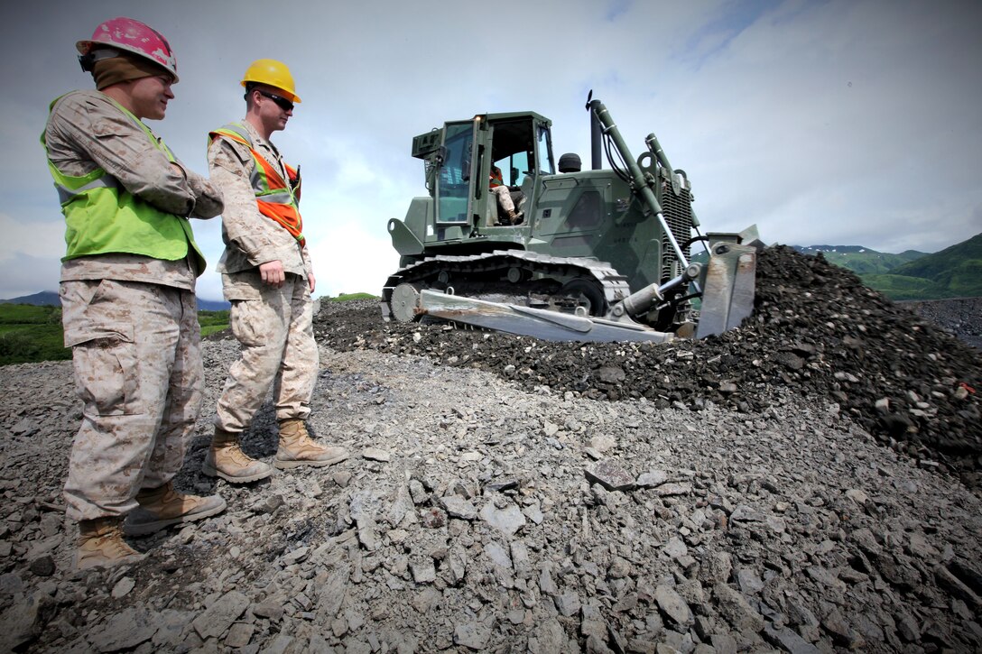 Sgt. Andrew Opsomer (right) and Cpl. Justin Bordaway, heavy equipment operators with Marine Wing Support Squadron 471,4th Marine Aircraft Wing, Marine Forces Reserve, supervise a Marine transporting gravel to dump trucks during the construction of an airstrip in Old Harbor, Alaska, July 11, 2014. Reserve Marines participating in Innovative Readiness Training Old Harbor extended the airstrip for the local population living on the island. (U.S. Marine Corps photo by Cpl. David Waite)