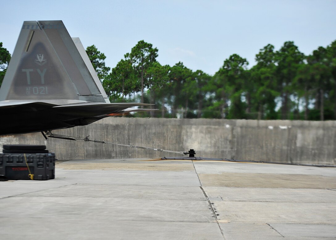 An F-22 Raptor is securely tethered to the center of an engine testing zone during the final phase for student maintainer certification 18 July during an operational engine run at Tyndall. Phase three is the culmination of academic, simulator and hands-on training after a prerequisite of six months airframe training and supervisor recommendation. (U.S. Air Force photo by Tech. Sgt. Javier Cruz/Released)