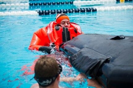 Petty Officer 3rd Class Toby Godwin, an instructor from the Naval Submarine School in Groton, Conn., assists a Naval Nuclear Power Training Command student as he practices survival techniques inside a Submarine Escape Immersion Equipment suit July 17, 2014, at Joint Base Charleston, S.C Almost 150 enlisted NNPTC students received training on surface survival techniques and using SEIE. (U.S. Air Force photo/Senior Airman George Goslin)