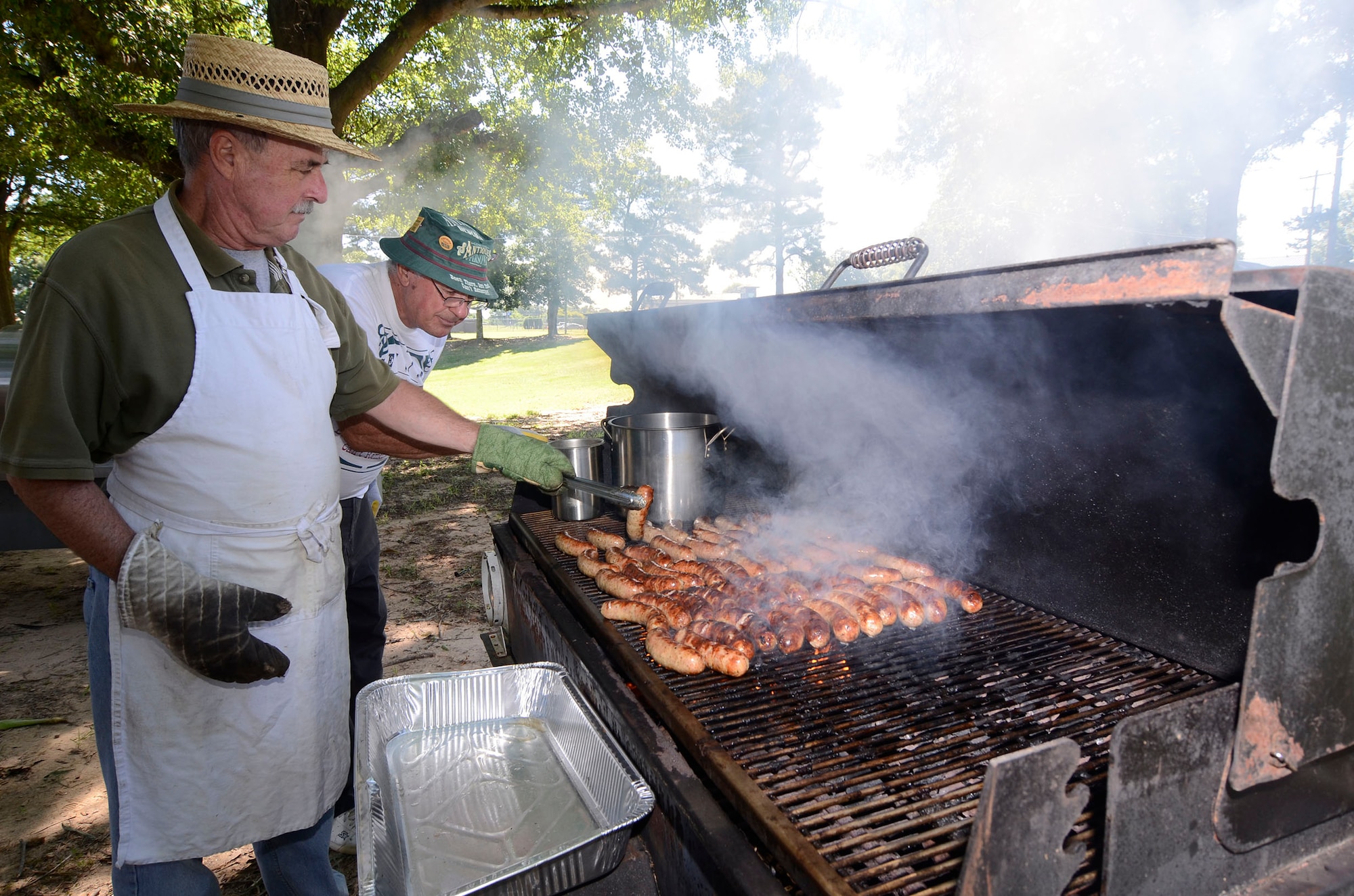 Lloyd Leinbaugh and Ron Durant attend to the grill as they prepare bratwursts for the 10th Annual Corn N’ Sausage Roast on Dobbins Air Reserve Base, Ga. July 16, 2014. The events proceeds are donated to the Airman and Family Readiness Emergency Fund. (U.S. Air Force photo/Don Peek)