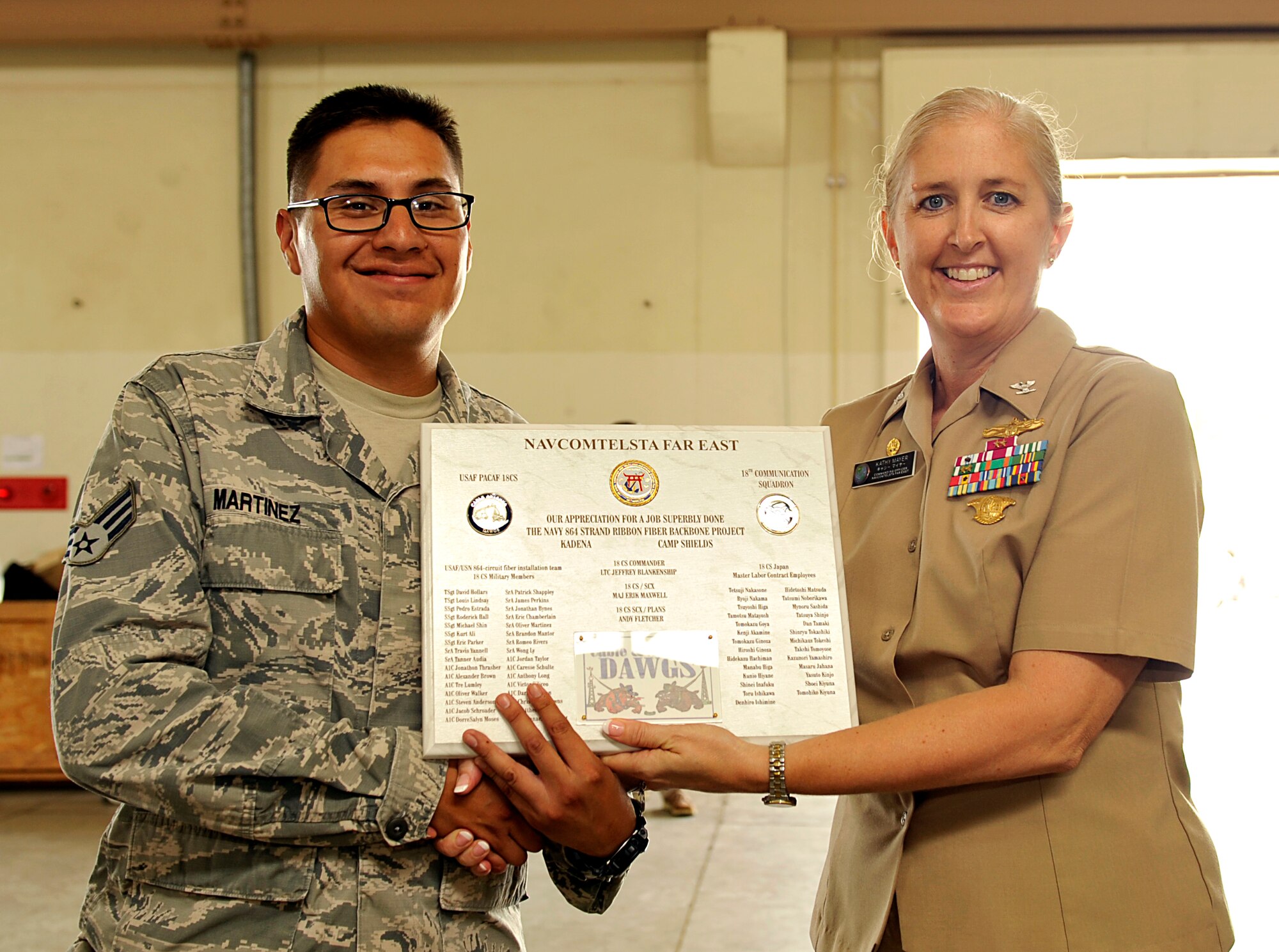 U.S. Air Force Senior Airman Oliver Martinez, 18th Communication Squadron cable and antenna system technician, receives a plaque from U.S. Navy Capt. Katherine Mayer, Naval Computer and Telecommunications Station Far East command officer, during a plaque presentation on Kadena Air Base, Japan, July 22, 2014. The 18th CS cable and antenna shop provided allied support during the installation of the Navy 864 circuit ribbon fiber optic cable, approximately 26,000 feet long, between Kadena Air Base and Camp Shields. The Navy 864 circuit ribbon fiber, significantly expands the IT backbone infrastructure between the two installations. (U.S. Air Force photo by Naoto Anazawa/Released)