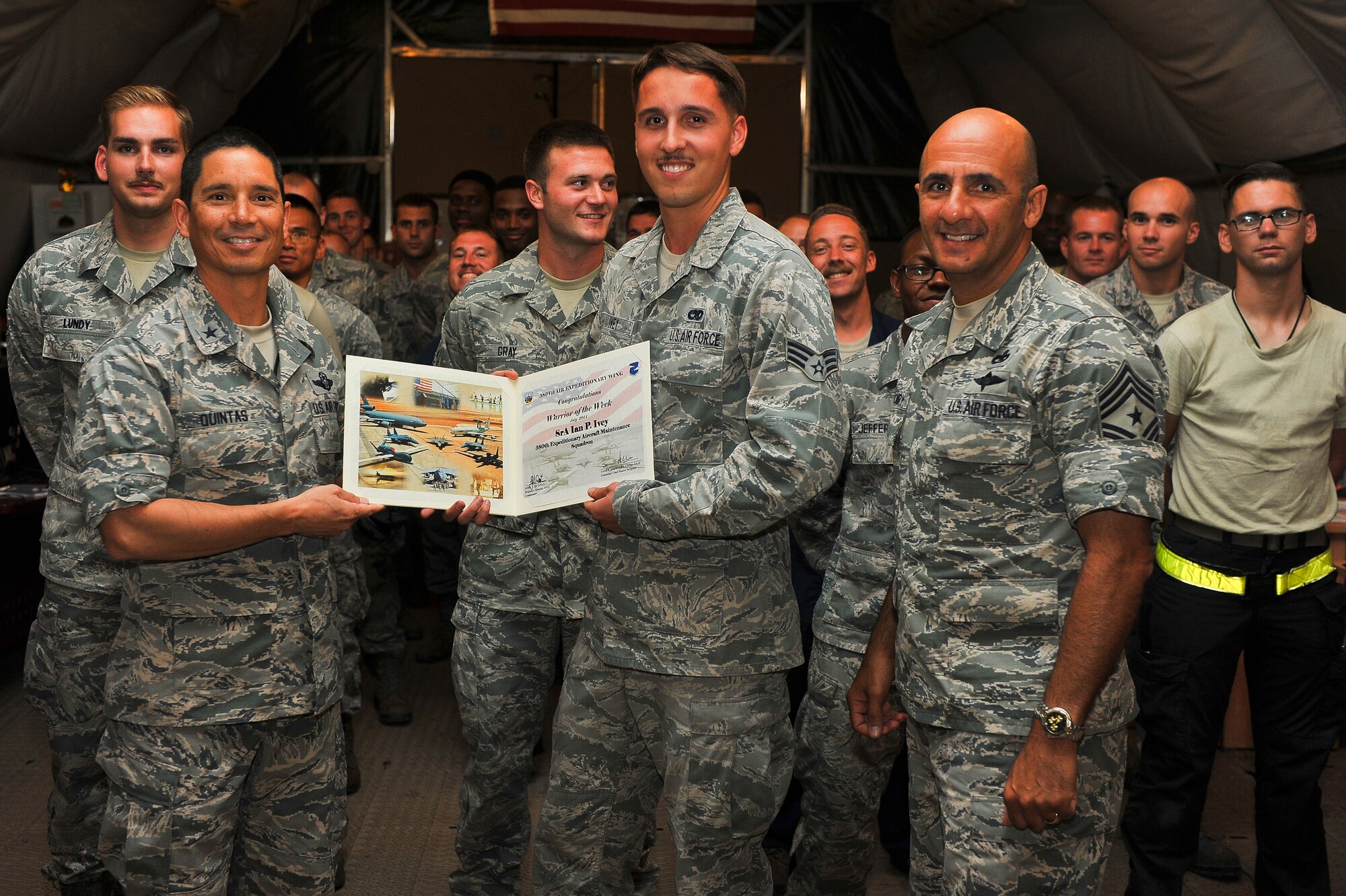 Air Force Brig. Gen. John T. Quintas, 380th Air Expeditionary Wing commander, and Chief Master Sgt.Samer Alkhoury, 380th Air Expeditionary Wing command chief, present Senior Airman Ian Ivey, 380th Expeditionary Maintenance Squadron, with a warrior of the week certificate July 24, 2014, at an undisclosed location in Southwest Asia. Ivey is a Belchertown, Ma., native, and is deployed from Joint Base Langley-Eustis, Va. (U.S. Air Force photo by Tech. Sgt. Russ Scalf/Released)