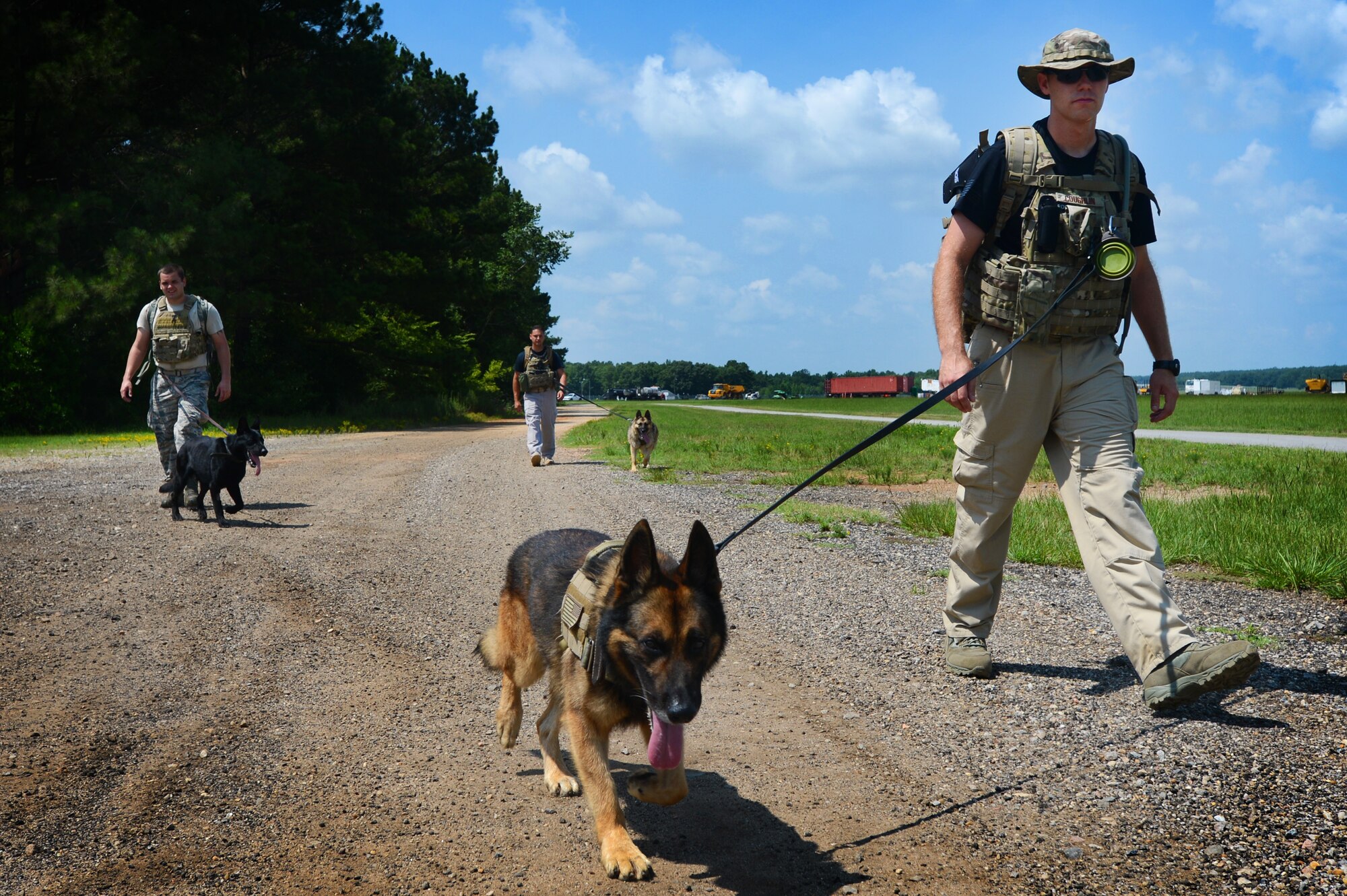 Three 20th Security Forces Squadron military working dog handlers walk with their K-9s during a training exercise at Shaw Air Force Base, S.C., July 24, 2014. During the more than five-mile walk, the Airmen carried 60-pound rucksacks while acclimating their K-9s to high temperatures and long walks which are likely common in deployed environments. (U.S. Air Force photo by Airman 1st Class Jensen Stidham/Released)