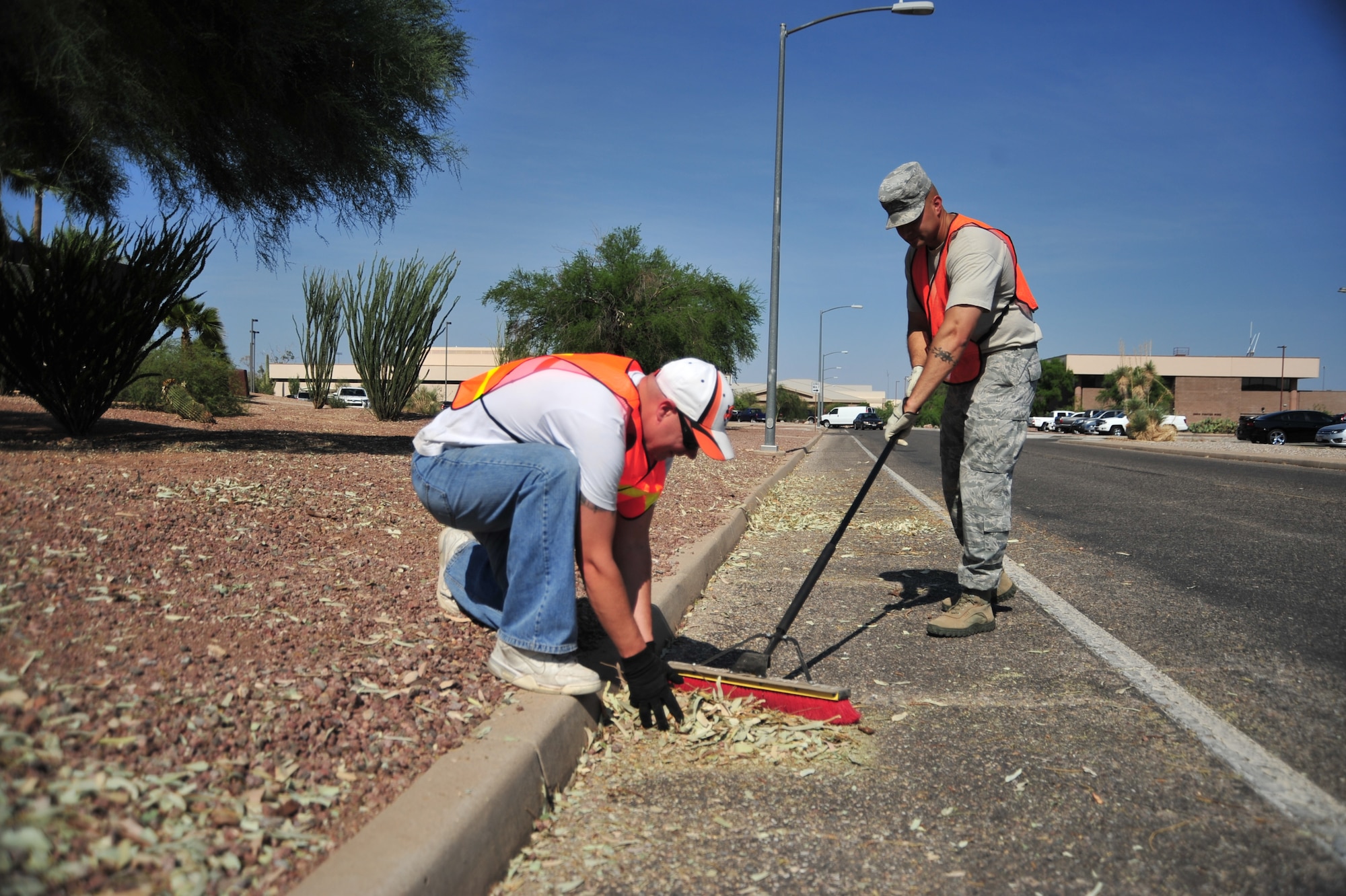 U.S. Air Force Tech. Sgt. Rodimez Brunner, 355th Force Support Squadron NCOIC of Fitness Assessment Cell, sweeps storm debris into a pile as Staff Sgt. Michael Feighery, 355th Force Support Squadron food service contracting officer representative, picks it up at Davis-Monthan Air Force Base Ariz., July 24, 2014.  Squadrons around D-M pitched in to help clean up debris caused by severe winds during a monsoon storm. (U.S. Air Force Photo by Airman 1st Class Chris Massey/Released)